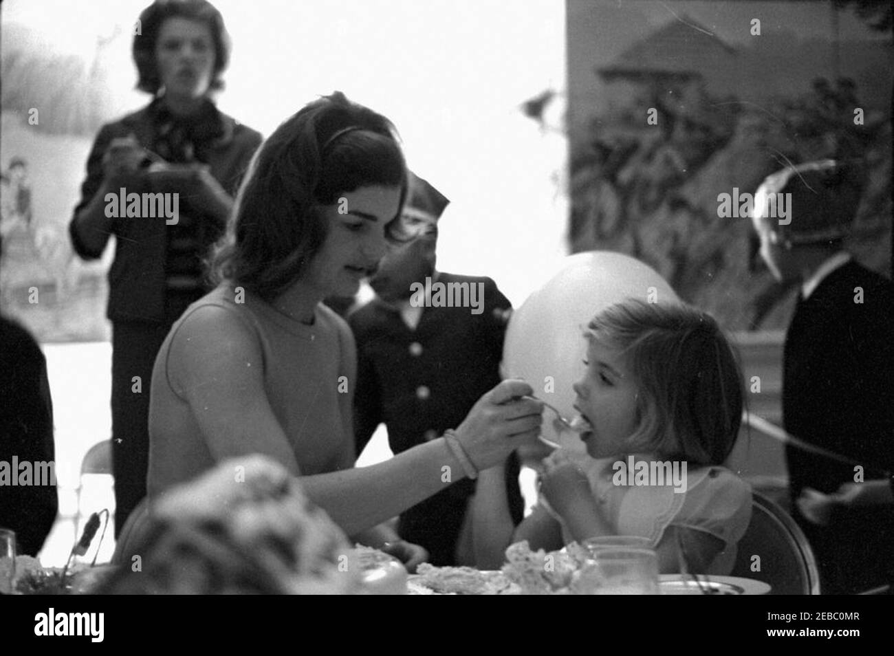 Fête d'anniversaire pour Caroline Kennedy et John F. Kennedy, Jr. La première dame Jacqueline Kennedy nourrit un morceau de gâteau à sa fille, Caroline Kennedy, lors d'une fête d'anniversaire conjointe pour Caroline et John F. Kennedy, Jr. Avery Hatcher, fils du Secrétaire de presse associé, Andrew T. Hatcher (partiellement caché), se tient au centre en arrière-plan. Presidentu2019s Dining Room (Residence), Maison Blanche, Washington, D.C. Banque D'Images Fête d'anniversaire pour Caroline Kennedy et John F. Kennedy, Jr. La première dame Jacqueline Kennedy nourrit un morceau de gâteau à sa fille, Caroline Kennedy, lors d'une fête d'anniversaire conjointe pour Caroline et John F. Kennedy, Jr. Avery Hatcher, fils du Secrétaire de presse associé, Andrew T. Hatcher (partiellement caché), se tient au centre en arrière-plan. Presidentu2019s Dining Room (Residence), Maison Blanche, Washington, D.C. Banque D'Images