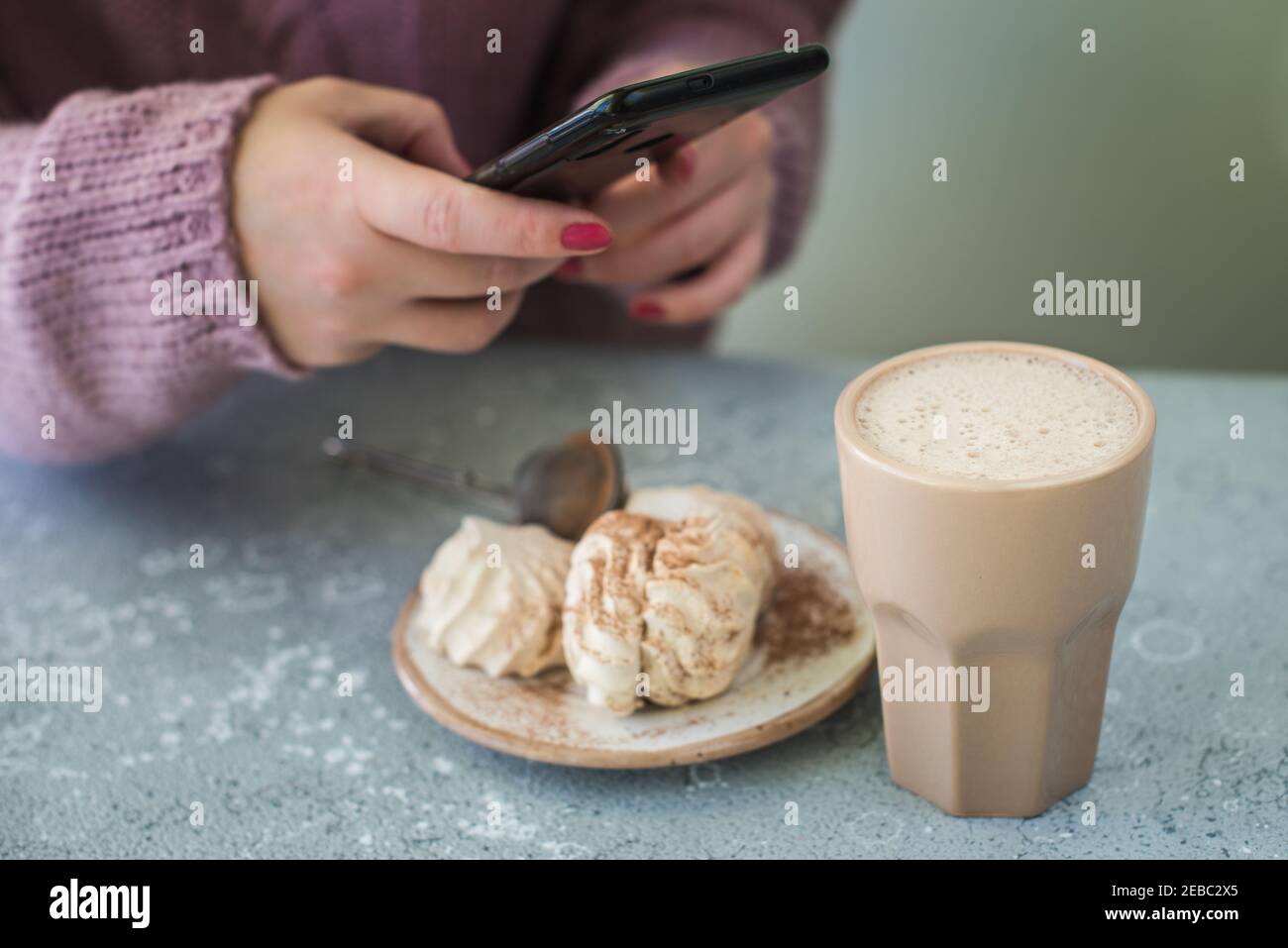 Une femme dans un chandail prend des photos de cacao et d'un gâteau sur un smartphone. Banque D'Images