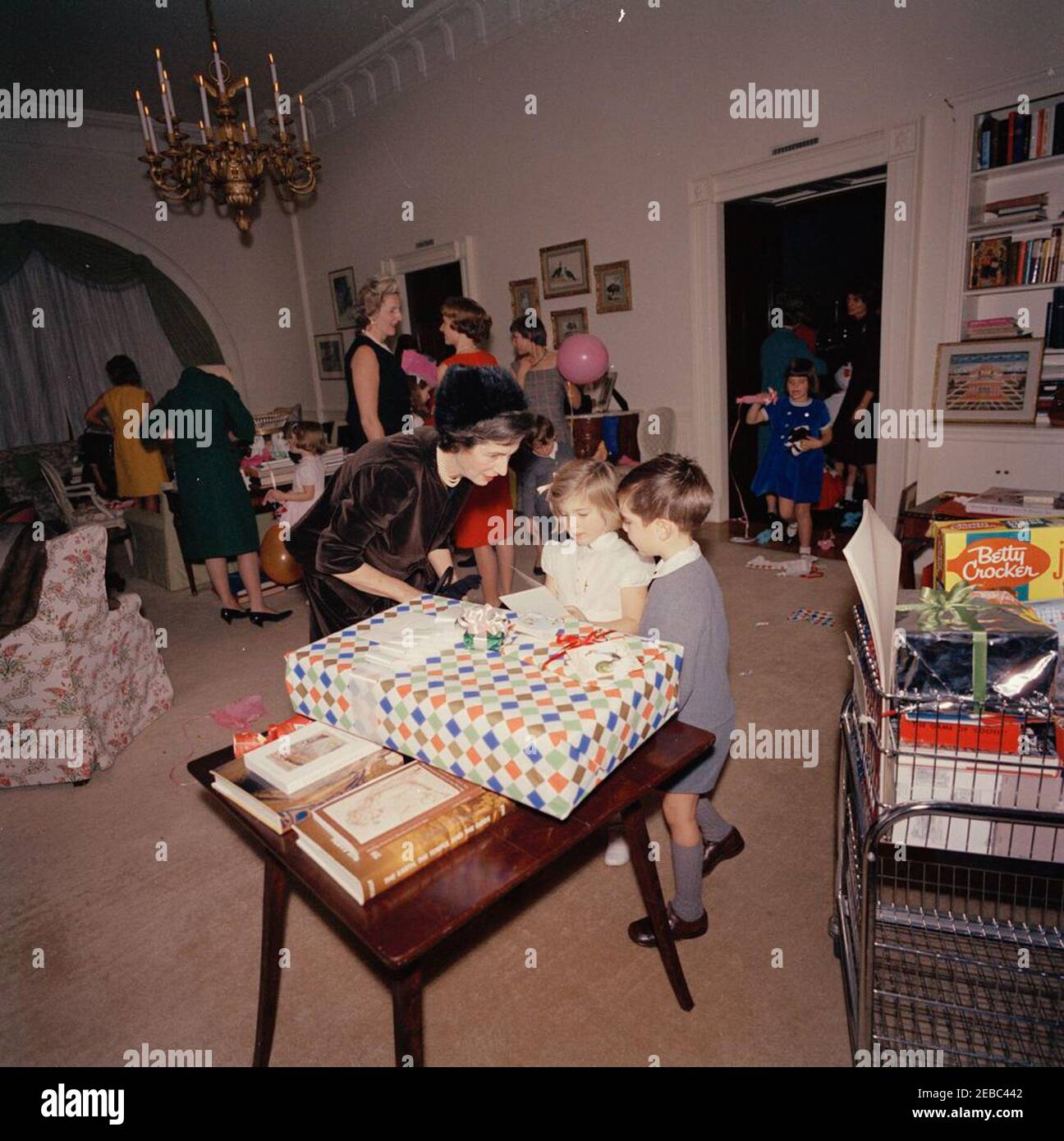 Fête d'anniversaire pour Caroline Kennedy et John F. Kennedy, Jr. Caroline Kennedy visite sa grand-mère, Janet Auchincloss, lors d'une fête d'anniversaire conjointe pour elle et son frère, John F. Kennedy, Jr.; plusieurs cadeaux sont assis sur la table en premier plan. Eunice Kennedy Shriver (principalement dans l'ombre) se tient à droite avec sa fille, Maria Shriver; la première secrétaire sociale Ladyu0027s, Letitia Baldrige (au centre à gauche), se tient en arrière-plan. West sitting Hall, Maison Blanche, Washington, D.C. Banque D'Images