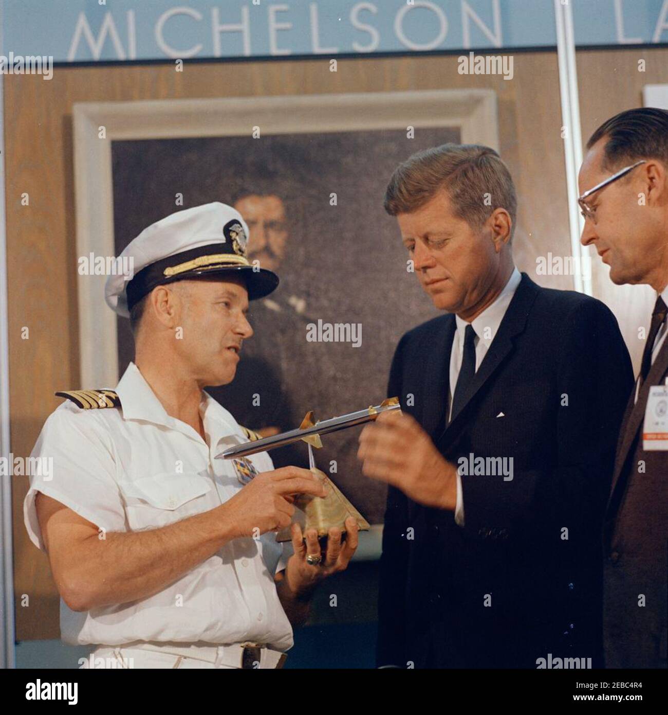 Voyage dans les États de l'Ouest : China Lake, Californie, (Naval Air Facility) NAF. Commandant de la station d'essais d'artillerie navale (NAF) à l'installation aérienne navale (NAF) China Lake en Californie, le capitaine Charles Blenman, Jr. (À gauche), présente au président John F. Kennedy un modèle du missile Shrike AGM-45 lors de sa visite au laboratoire NOTSu0027 Michelson; LE DIRECTEUR technique DE NOTS, le Dr William B. McLean, est à droite. Un portrait du physicien, Albert A. Michelson, est suspendu sur le mur en arrière-plan. [Notes: Voir aussi Mo 63.1920, u0022Model of AGM-45 Shrike Missileu0022, du John F. Kennedy Admins Banque D'Images