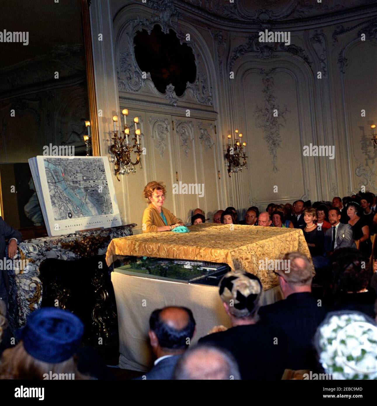 La première dame voit le modèle du Centre culturel national de Newport, Rhode Island. L'actrice Geraldine page (debout au centre), parle lors du dévoilement d'un modèle architectural du Centre culturel national lors d'une cérémonie au manoir Elms de Newport, Rhode Island; la première dame Jacqueline Kennedy est assise en première rangée derrière le modèle. Les personnes assises derrière le modèle comprennent également : la présidente du Comité de campagne de la région de Washington pour le Centre culturel national, Janet Auchinclors; la directrice musicale de l'Orchestre symphonique de Boston, Erich Leinsdorf; l'architecte, Edward Durell Stone; membre de l'A Banque D'Images
