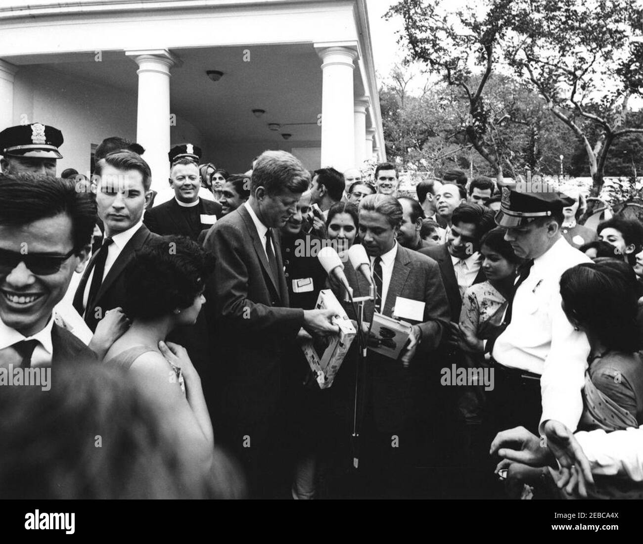 Visite des participants à l'expérience dans International Living, 12:00. Le président John F. Kennedy (à gauche des microphones) fait un cadeau lors d'une visite des participants au programme expérience de vie internationale. Asha Mirchandani, de l'Inde (qui a présenté au président Kennedy une photo en marbre de la première dame Jacqueline Kennedy), se tient à droite du président, partiellement caché. Toby Chandler, agent du service secret de la Maison Blanche, se trouve à gauche; d'autres sont non identifiés. West Wing Lawn, Maison Blanche, Washington, D.C. Banque D'Images