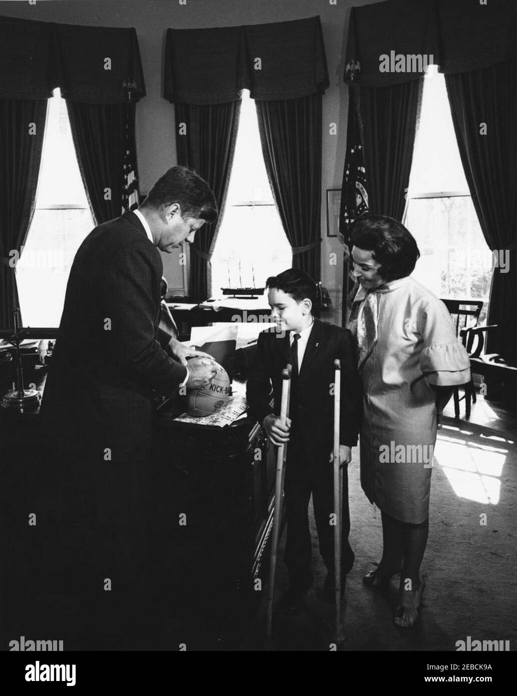 Visite de Thomas A. Doyle, III, 1962 Easter Seal Child, 12:07PM. Le président John F. Kennedy signe un ballon de kick pour Thomas A. Doyle, III (au centre), l'enfant de Pâques 1962. Pauline Phillips (chroniqueur de journaux Abigail Van Buren, ou u201cChère Abbyu201d), présidente de l'entraînement du Sceau de Pâques, parrainée par la Société nationale pour les enfants et les adultes handicapés. Oval Office, Maison Blanche, Washington, D.C. Banque D'Images