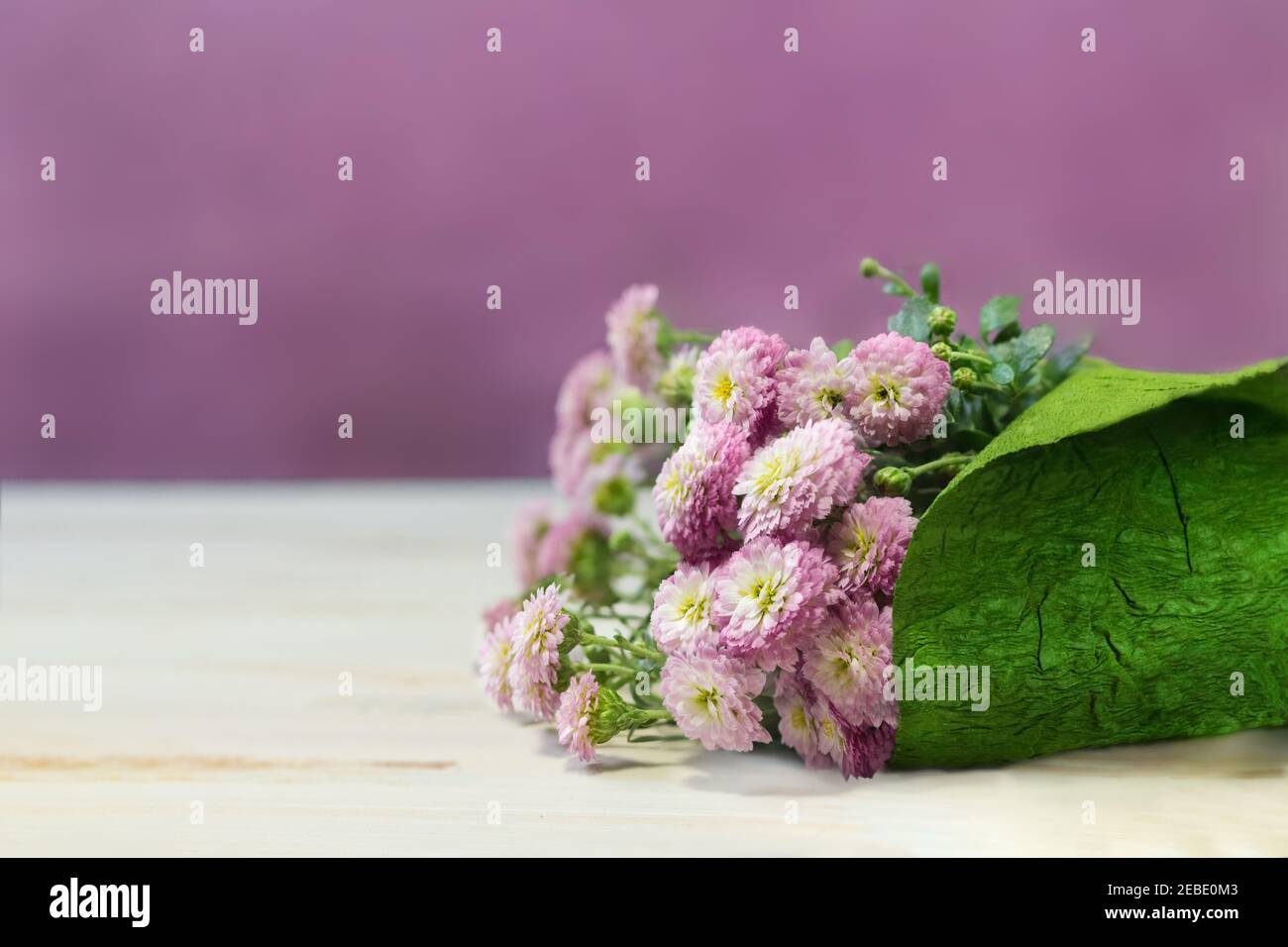 Bouquet de fleurs en papier d'emballage vert. Petits chrysanthèmes blancs et roses sur la table. Présent. Copier l'espace Banque D'Images