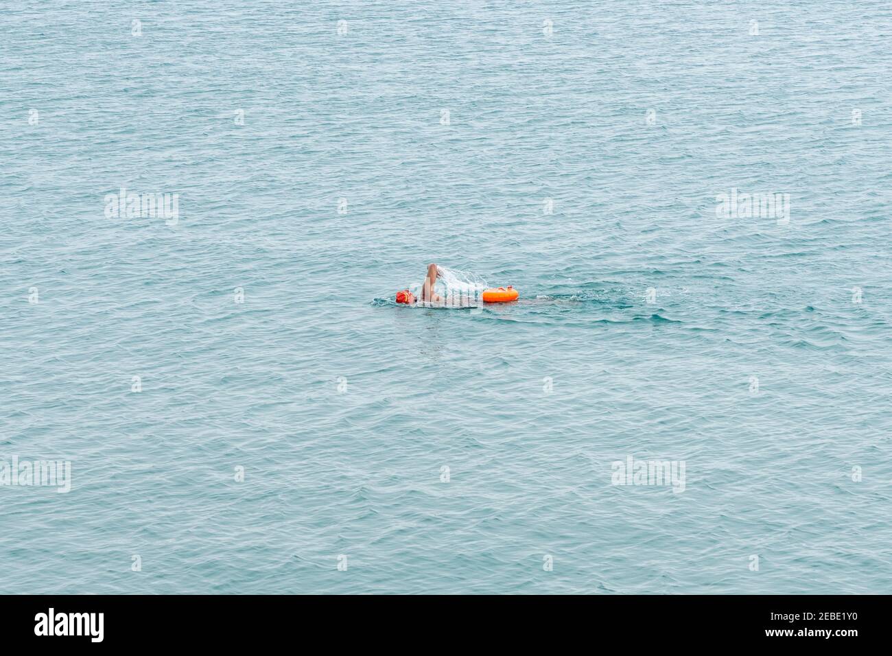 Nageur longue distance avec casquette orange et sac de natation sec dans l'eau de mer ouverte sans fin Banque D'Images