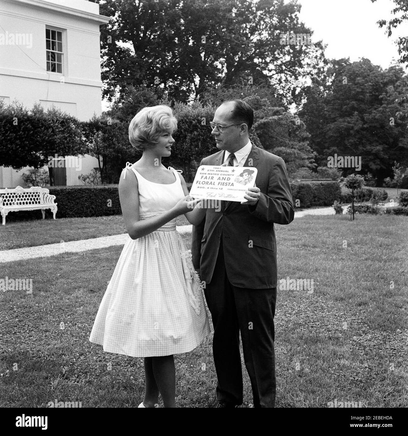 Planter une rosier à la Maison Blanche. Planter une rosier à la Maison Blanche. Une femme non identifiée présente l'assistant spécial du président Frederick G. Dutton avec des panneaux pour la foire et la fête florale du comté de San Mateo (Californie). Aile est, Maison Blanche, Washington, D.C. Banque D'Images