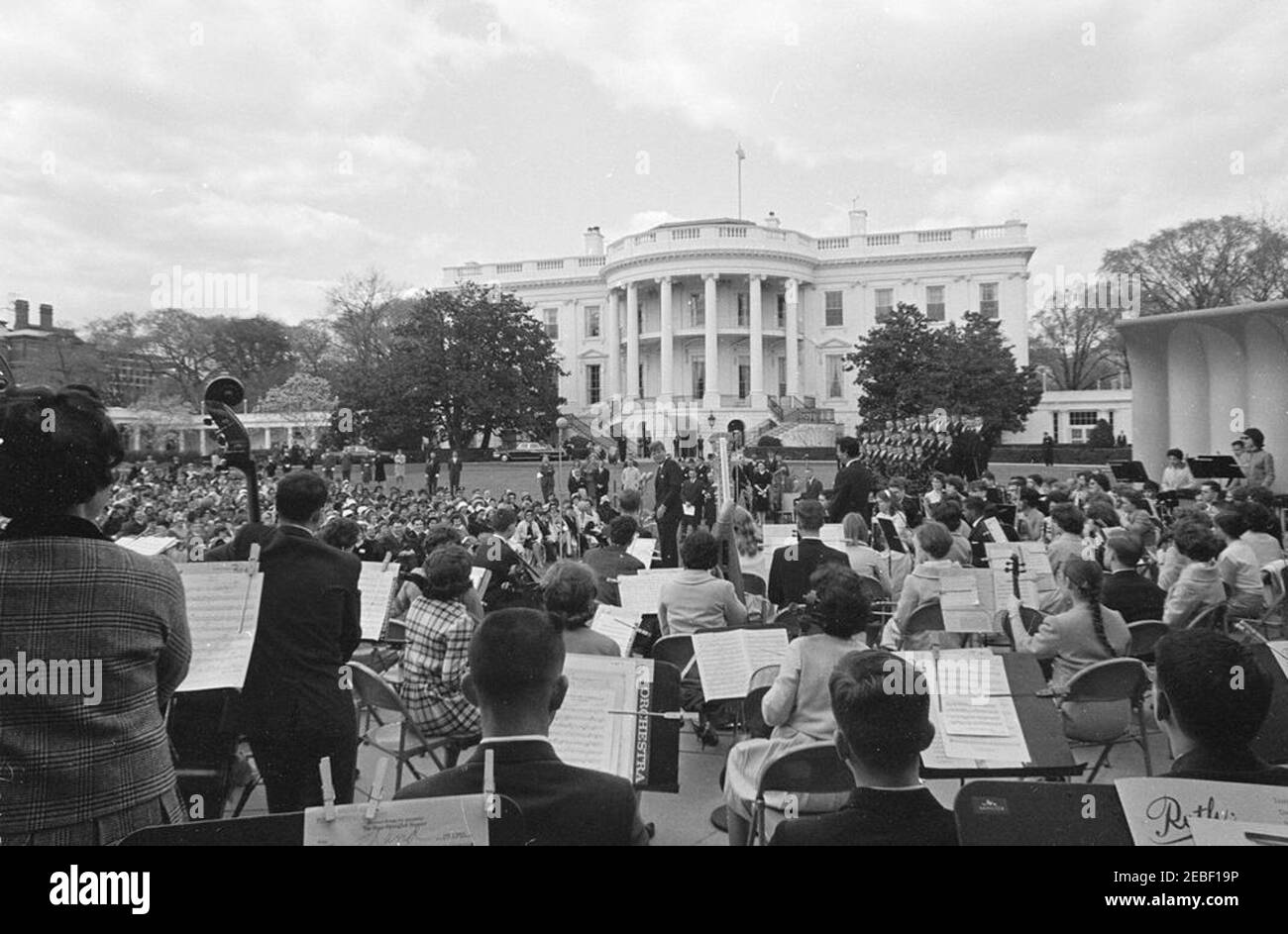 Programme musical pour les jeunes de la première Dame Jacqueline Kennedyu0027s (JBK), 14 h 35. Le président John F. Kennedy (au centre, en arrière-plan) fait des remarques au cours de la troisième série de programmes musicaux pour les jeunes par les jeunes de la première Dame Jacqueline Kennedyu0027s. Le chef du Greater Boston Youth Symphony Orchestra (GBYSO), le Dr Marvin Rabin (au centre à droite, à l'arrière de la caméra), est sur scène avec l'orchestre; les membres du Breckenridge Boys Choir se tiennent en formation à gauche de la scène. South Lawn, Maison Blanche, Washington, D.C. Banque D'Images