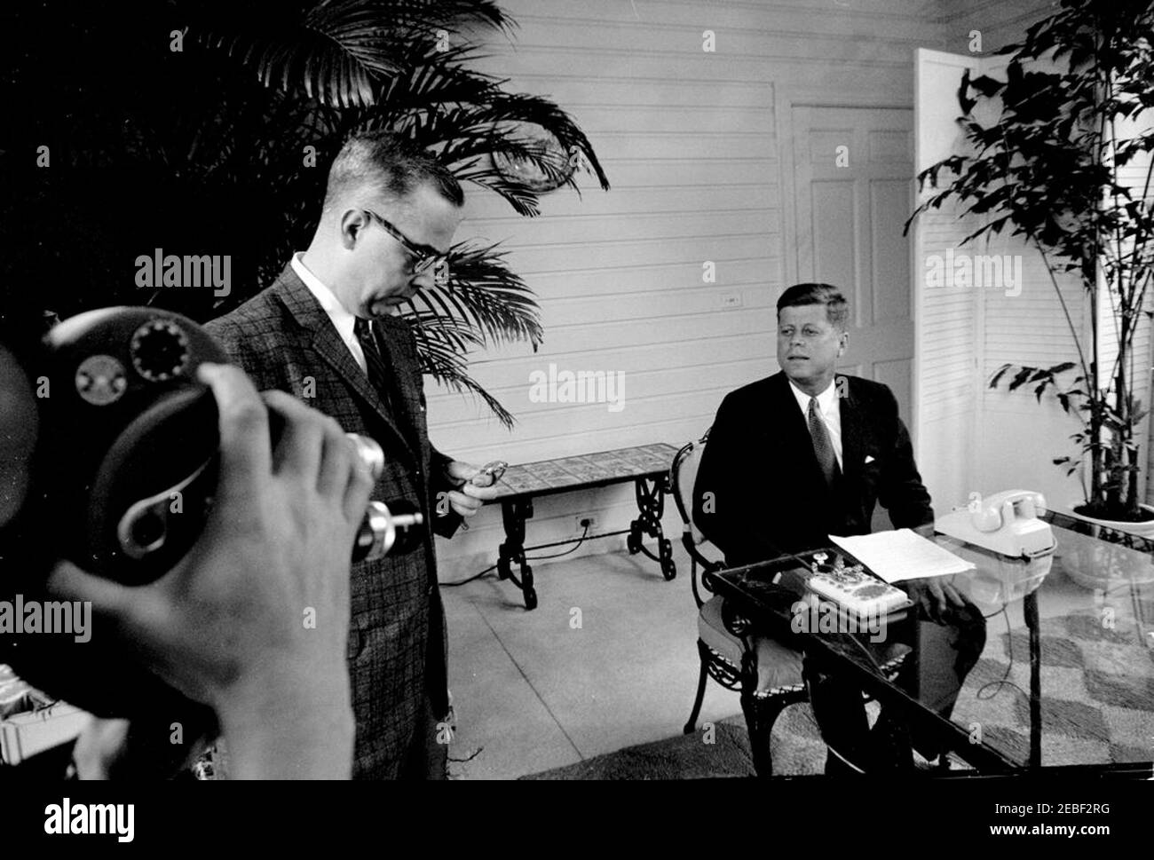 Cérémonie d'ouverture de la foire de Seattle Worldu0027s au départ de Palm Beach. Le président John F. Kennedy s'assoit à une table de patio en préparation de la cérémonie d'ouverture de la foire de Seattle Worldu0027s de 1962 (également connue sous le nom de Century 21 exposition) depuis la résidence de C. Michael Paul à Palm Beach, en Floride. Robert Bright, de l'American Telephone and Telegraph Company (ATu0026T), se trouve à gauche, vérifiant une montre; un caméraman non identifié (sur le bord du cadre) films à gauche. Le président Kennedy a prononcé des remarques par téléphone et a appuyé sur une touche de télégraphe en or (sur la table) pour ouvrir la foire par signal satellite Banque D'Images Cérémonie d'ouverture de la foire de Seattle Worldu0027s au départ de Palm Beach. Le président John F. Kennedy s'assoit à une table de patio en préparation de la cérémonie d'ouverture de la foire de Seattle Worldu0027s de 1962 (également connue sous le nom de Century 21 exposition) depuis la résidence de C. Michael Paul à Palm Beach, en Floride. Robert Bright, de l'American Telephone and Telegraph Company (ATu0026T), se trouve à gauche, vérifiant une montre; un caméraman non identifié (sur le bord du cadre) films à gauche. Le président Kennedy a prononcé des remarques par téléphone et a appuyé sur une touche de télégraphe en or (sur la table) pour ouvrir la foire par signal satellite Banque D'Images