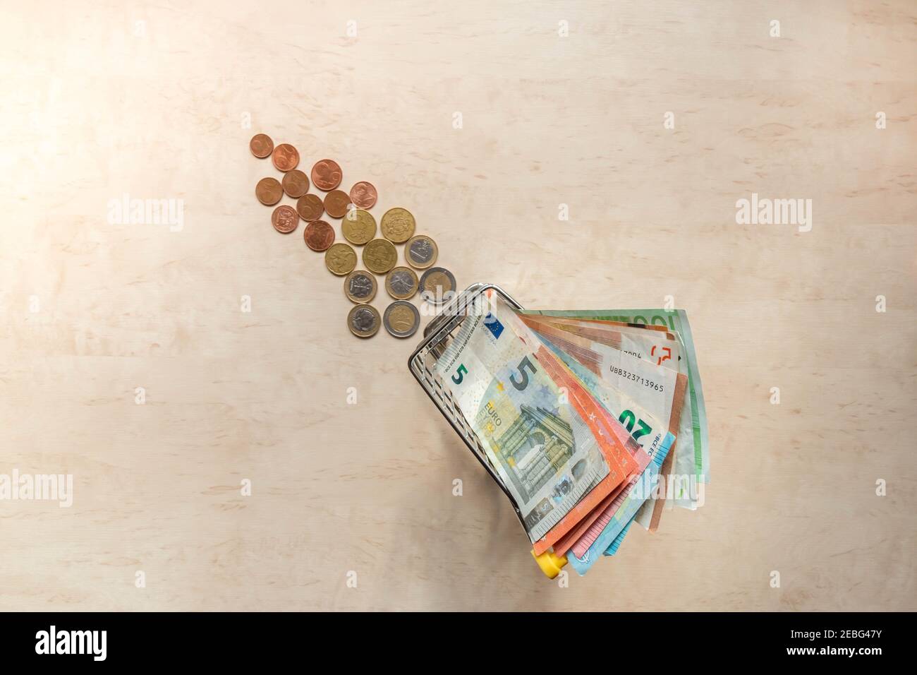 Billets en euros dans un petit panier et pièces en euros en arrière-plan. Petit chariot de shopping avec argent. Monnaie de la zone euro. Copier l'espace. Vue de dessus. Hai Banque D'Images