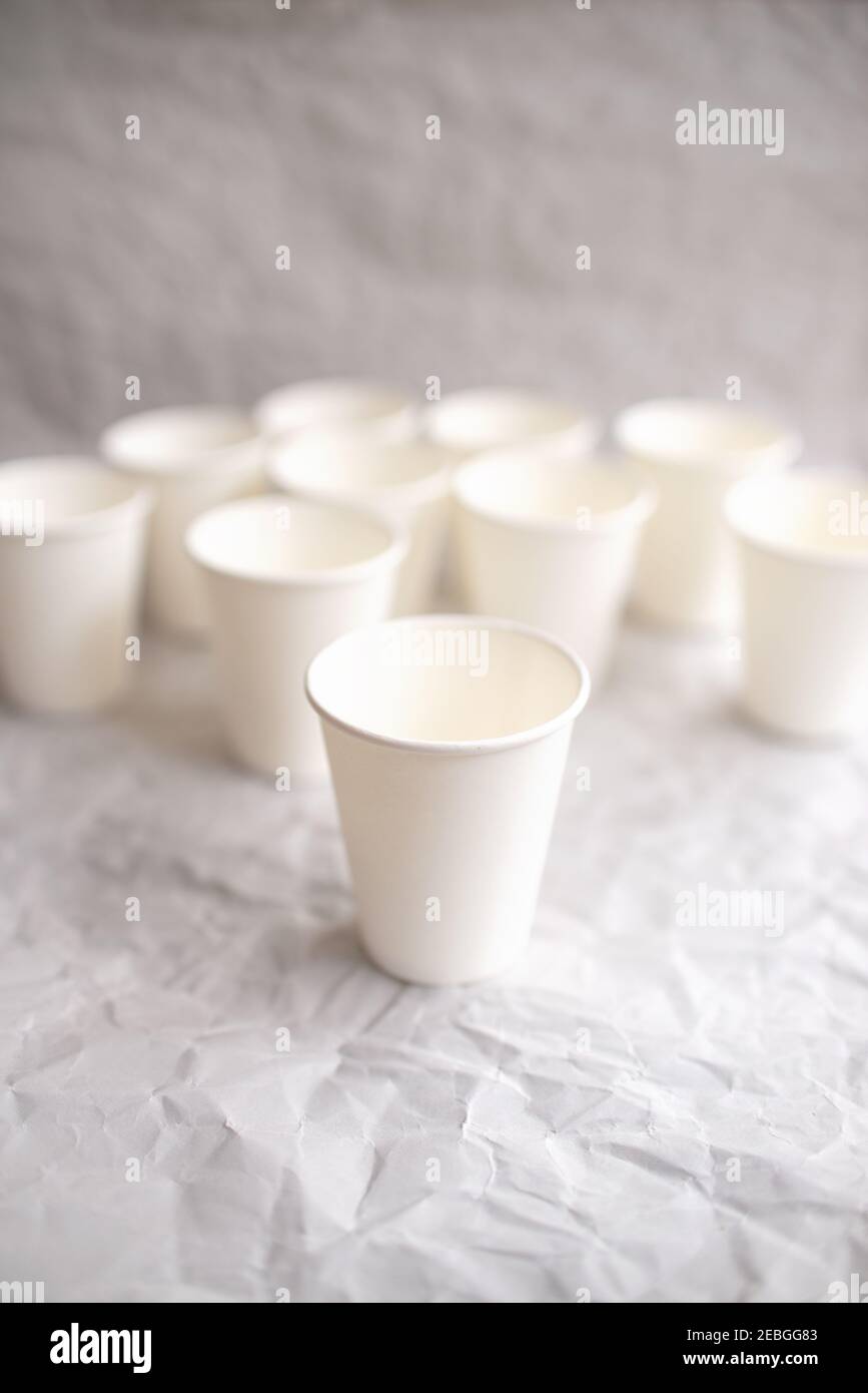 des tasses jetables en papier blanc sont disposées sur papier gris froissé selon un motif géométrique Banque D'Images