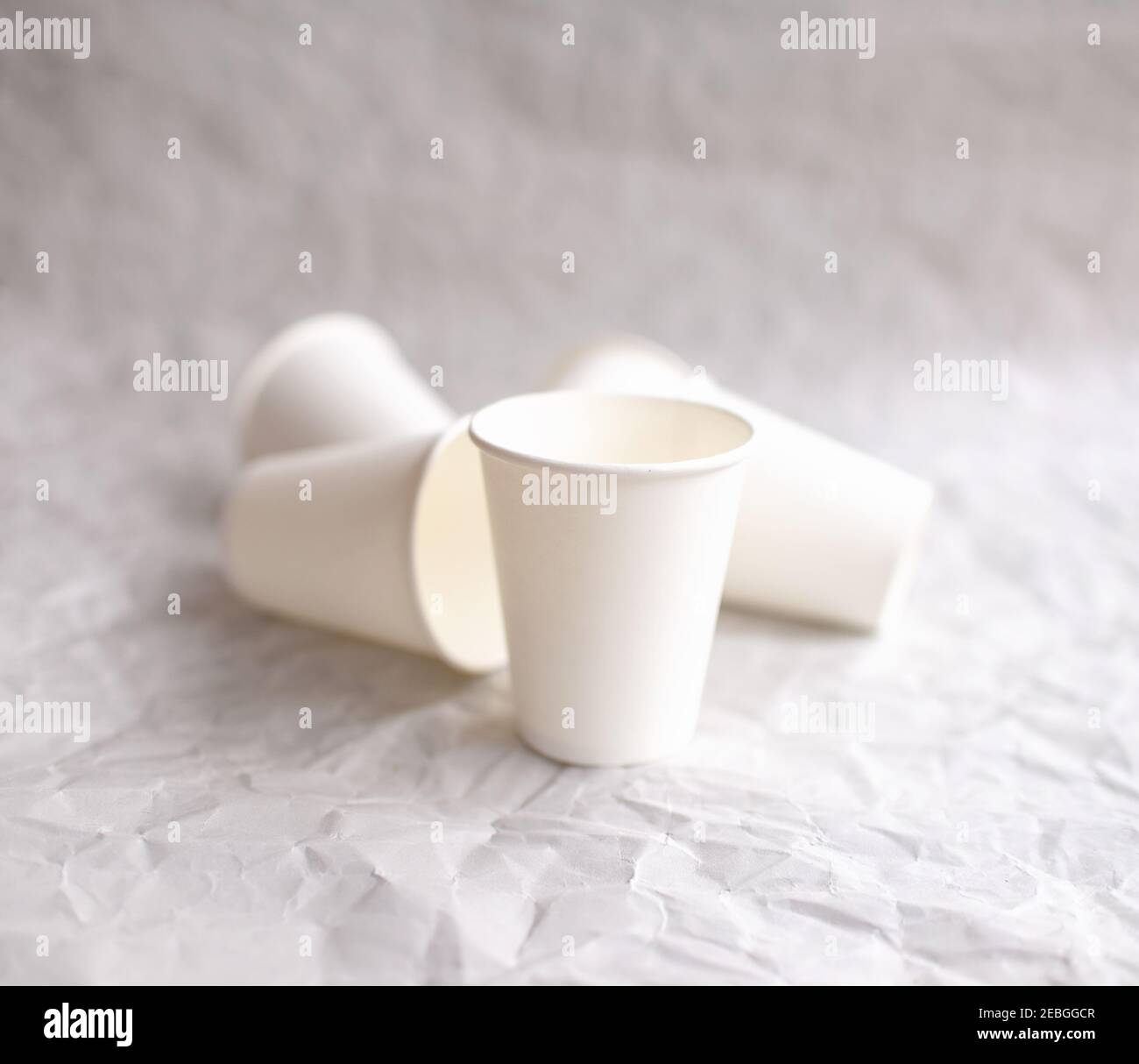des tasses jetables en papier blanc sont disposées sur papier gris froissé selon un motif géométrique Banque D'Images