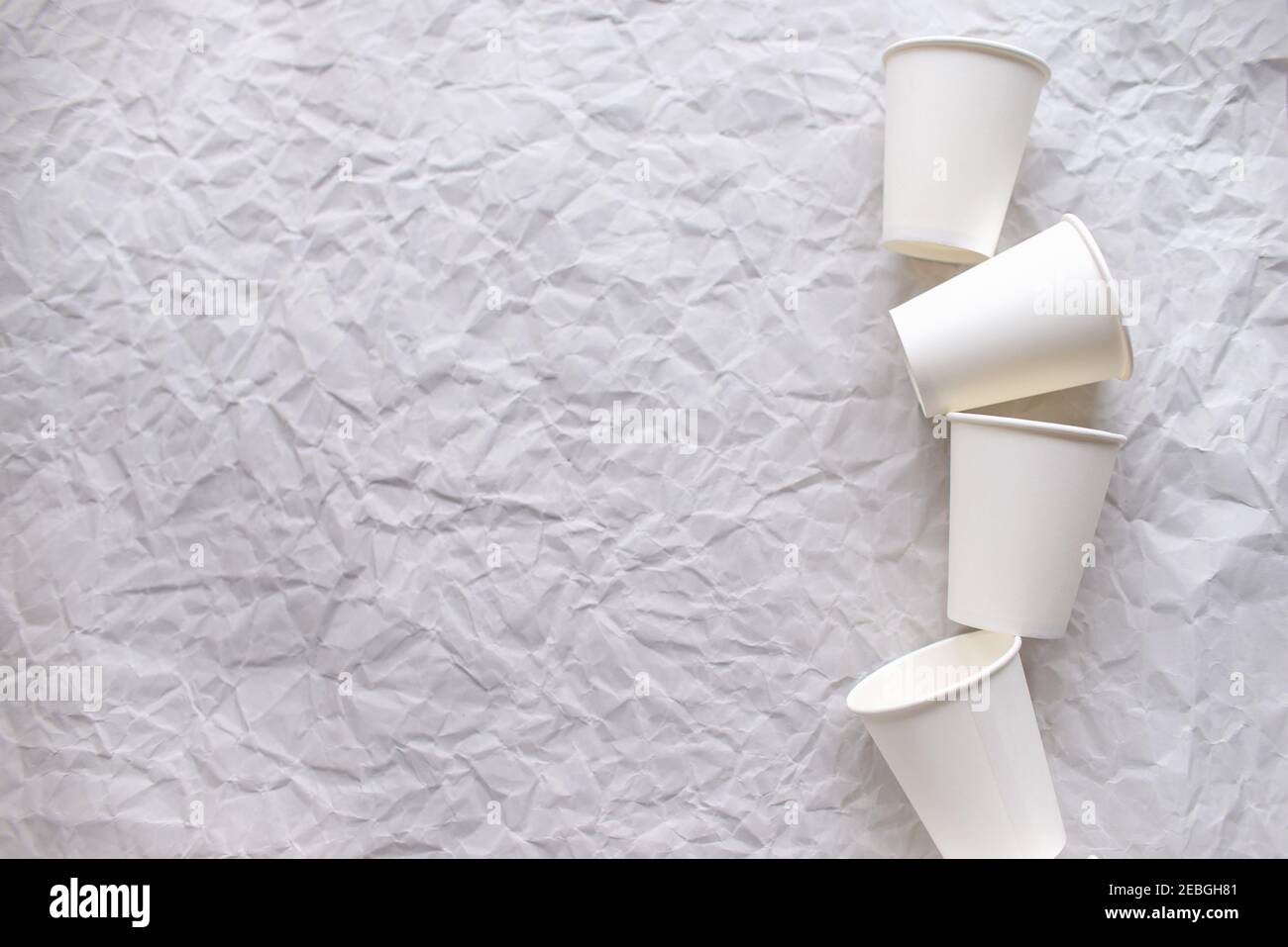 des tasses jetables en papier blanc sont disposées sur papier gris froissé selon un motif géométrique Banque D'Images