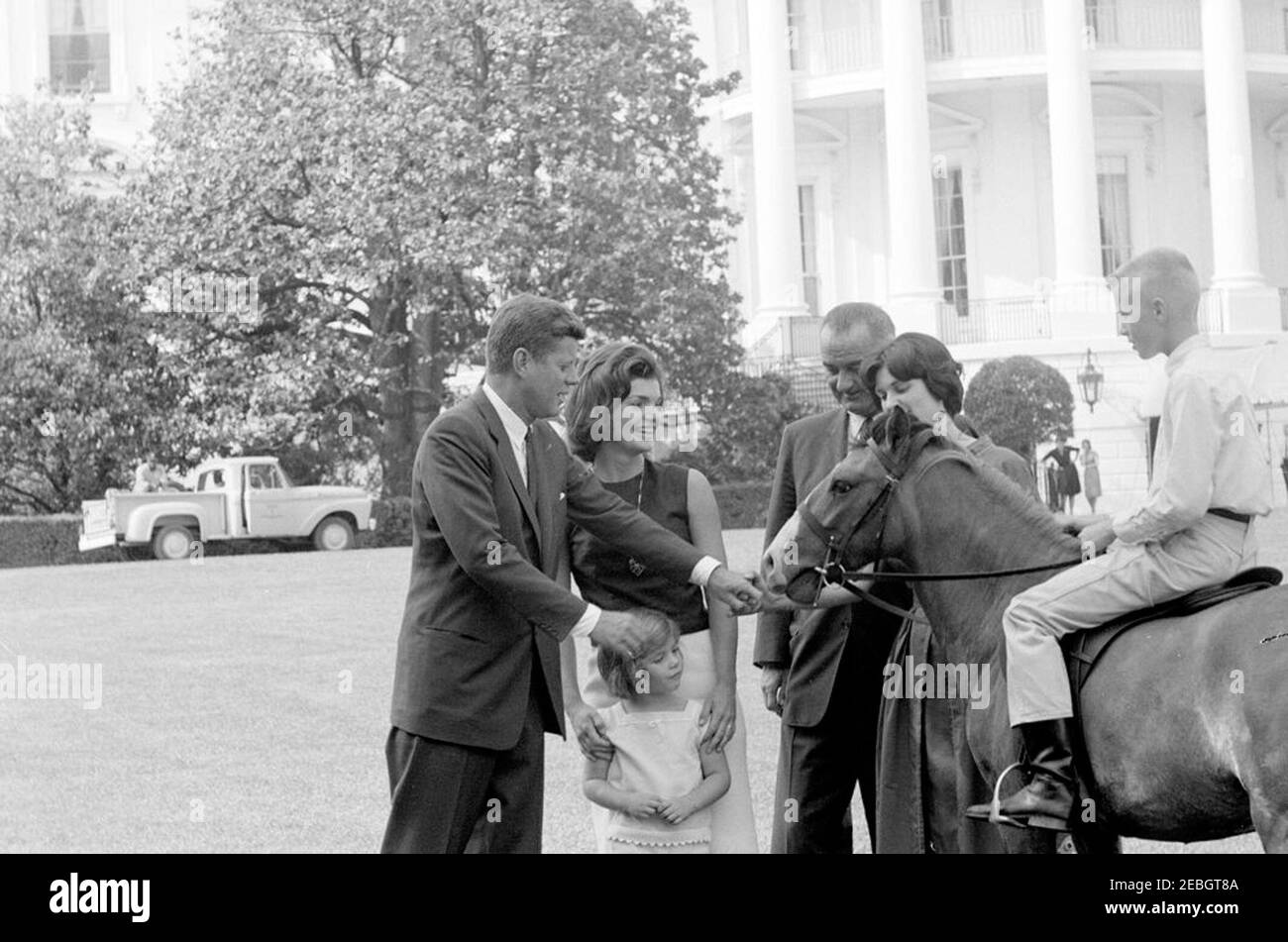 Le vice-président Lyndon B. Johnson (LBJ) présente un nouveau poney, u201cTexu201d à Caroline Kennedy (CBK); les enfants jouant sur la pelouse du Sud. Le président John F. Kennedy, la première dame Jacqueline Kennedy, et Caroline Kennedy ont visité le vice-président Lyndon B. Johnson et Lynda Bird Johnson (qui se sont joints au président Kennedy) sur la pelouse sud de la Maison Blanche. Un garçon non identifié est assis à bord de Tex, un poney donné à Caroline comme cadeau du vice-président Johnson. Washington, D.C. Banque D'Images