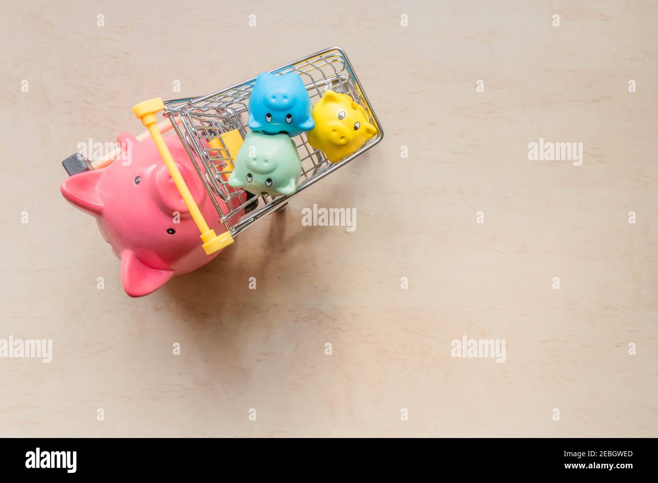 Grande banque de cochons tenant un panier avec des petits bancs de cochons sur fond de bois. Une grande banque de porcs roulant trois banques de porcelets dans un chariot. Banques de cochons i Banque D'Images