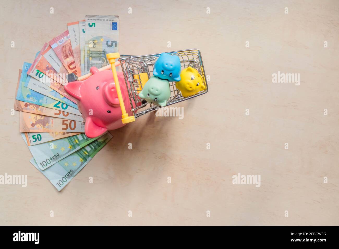 Une grande banque de cochons roulant trois petites banques de cochons dans un chariot sur fond de bois avec des billets en euros. Banques de gros porcs et de porcelets, billets en euros et s Banque D'Images