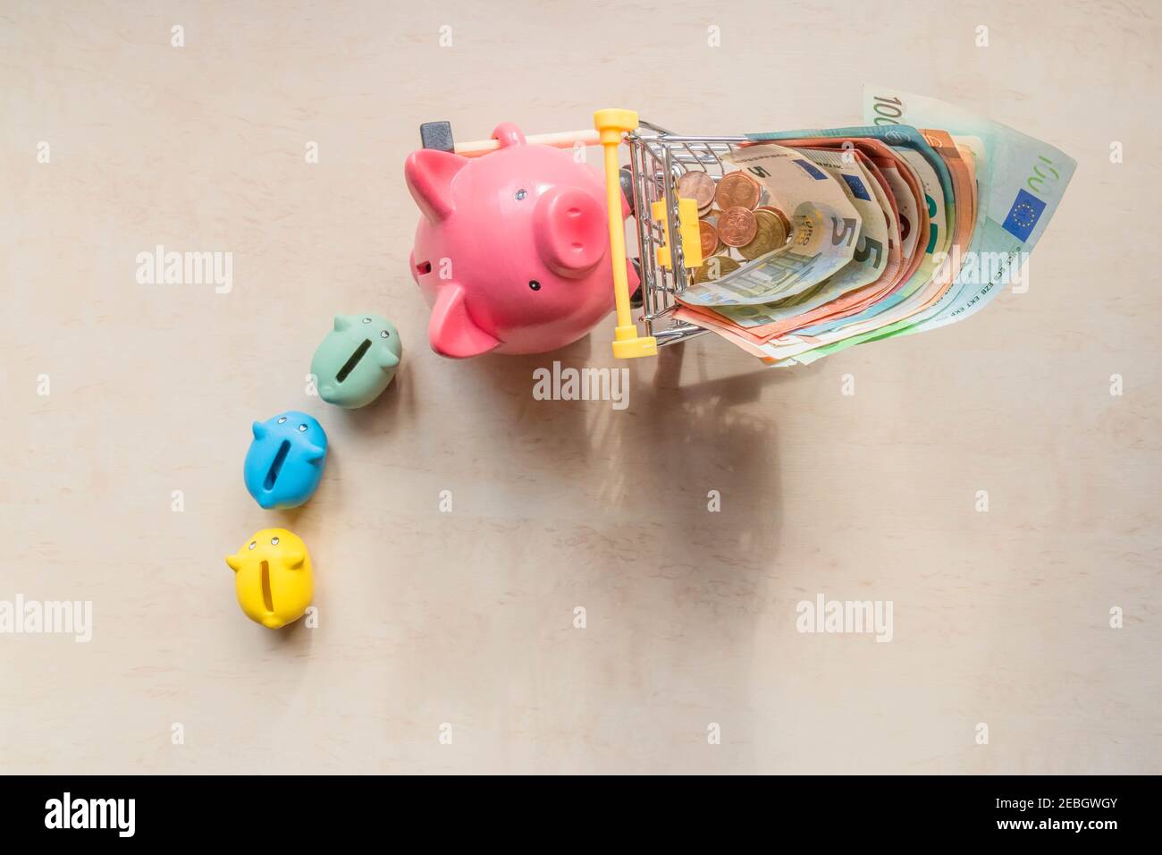 Les banques de porcelets suivent une grande banque de cochons, qui roule avec des billets en euros sur fond de bois. Gros cochon, petites banques de cochons et billets en euros en s. Banque D'Images