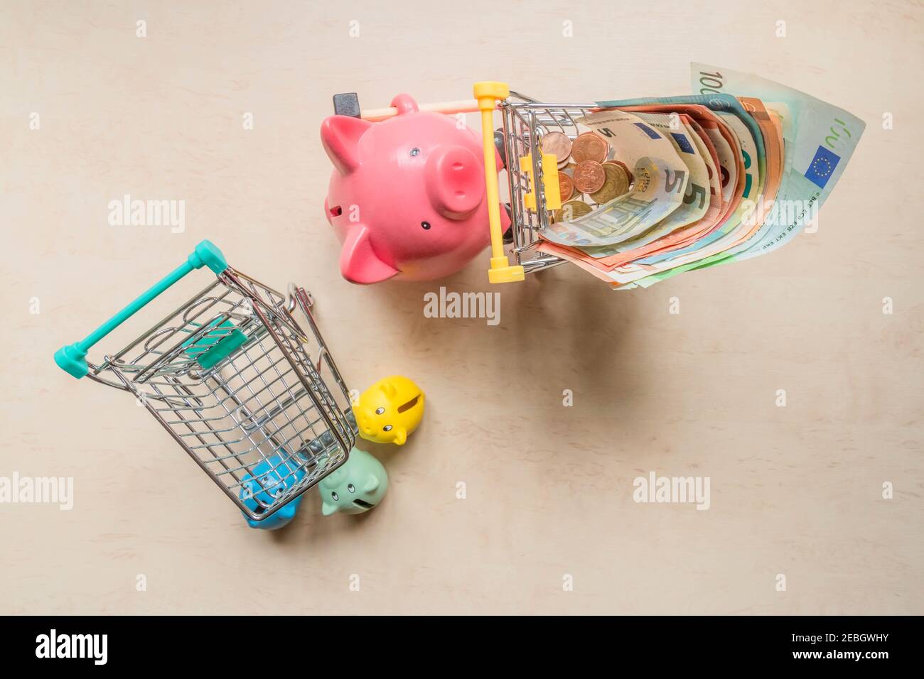 Chariot roulant de grande banque de cochons avec billets en euros et petites banques de cochons tenant un chariot vide. Les banques de porcelets avec un panier vide et un gros cochon Banque D'Images