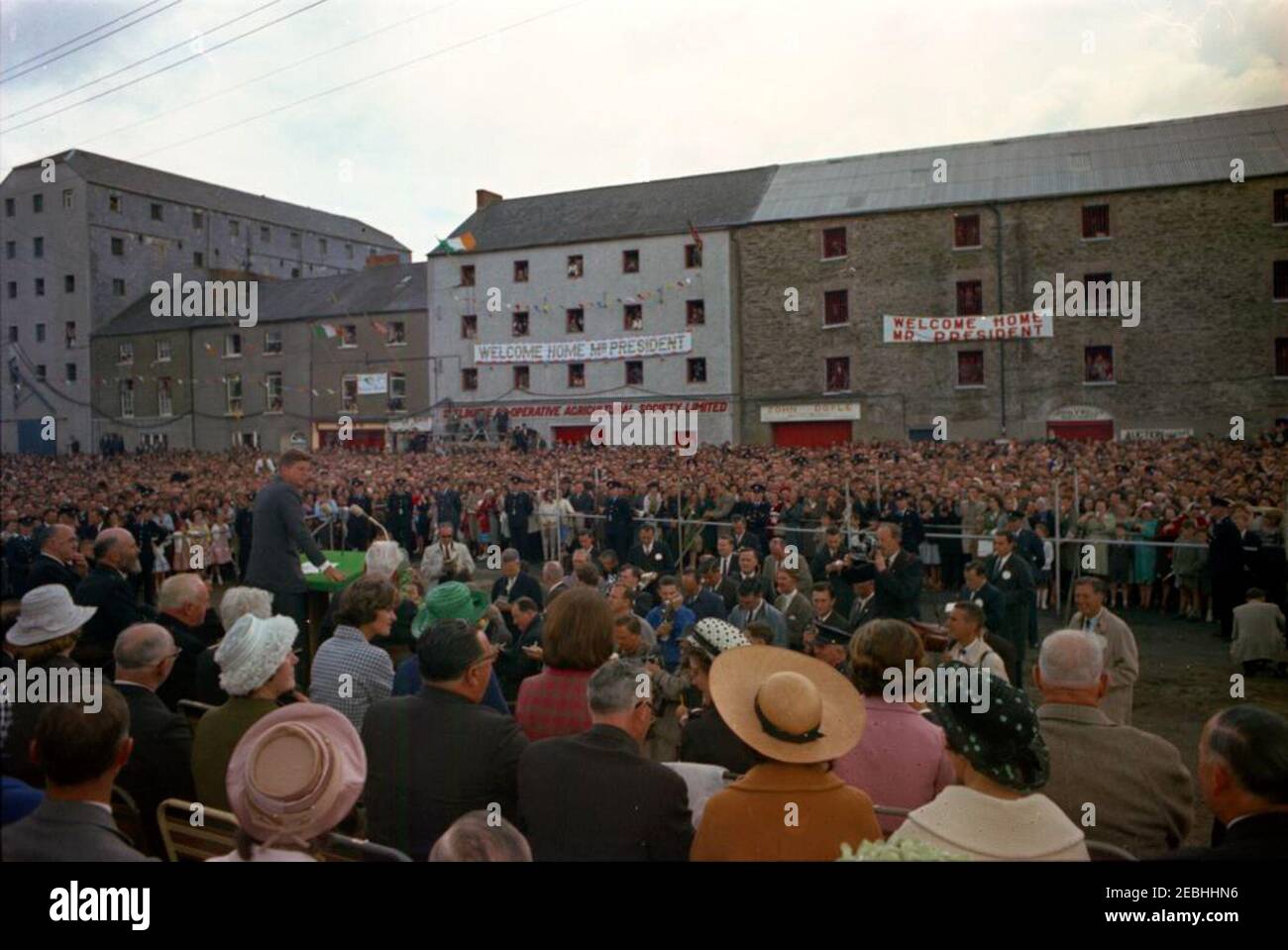 Voyage en Europe: Irlande, New Ross. Le président John F. Kennedy (à gauche, au pupitre) prononce un discours devant la foule rassemblée à New Ross Quay, dans le comté de New Ross, en Irlande, le port d'où son arrière-grand-père Patrick Kennedy a émigré aux États-Unis. Reporters et photographes observent la plate-forme speakersu0027 ci-dessous; également photographié (assis sur la plate-forme speakersu0027): Le ministre des Affaires extérieures de l'Irlande, Frank Aiken; le président du conseil du district urbain de New Ross, Andrew Minihan; le vice-président du conseil du district urbain de New Ross, Gerald Donovan; le président Ken Banque D'Images