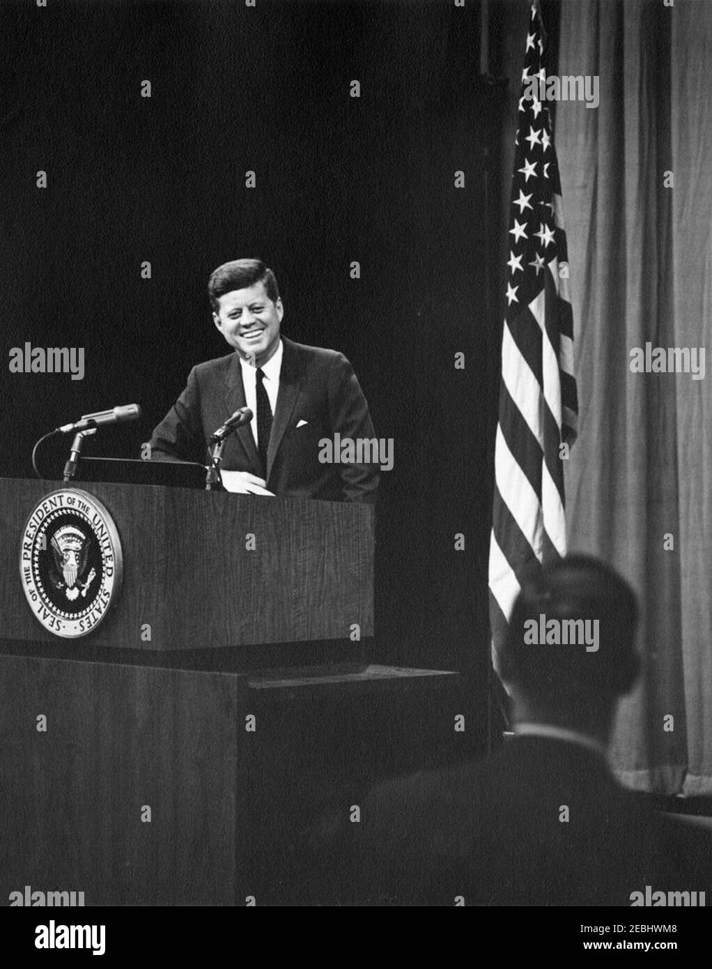 Conférence de presse à l'Auditorium du Département d'État, 6:00. Le président John F. Kennedy rit tout en écoutant la question d'un journaliste non identifié. Auditorium du département d'État, Washington, D.C. Banque D'Images