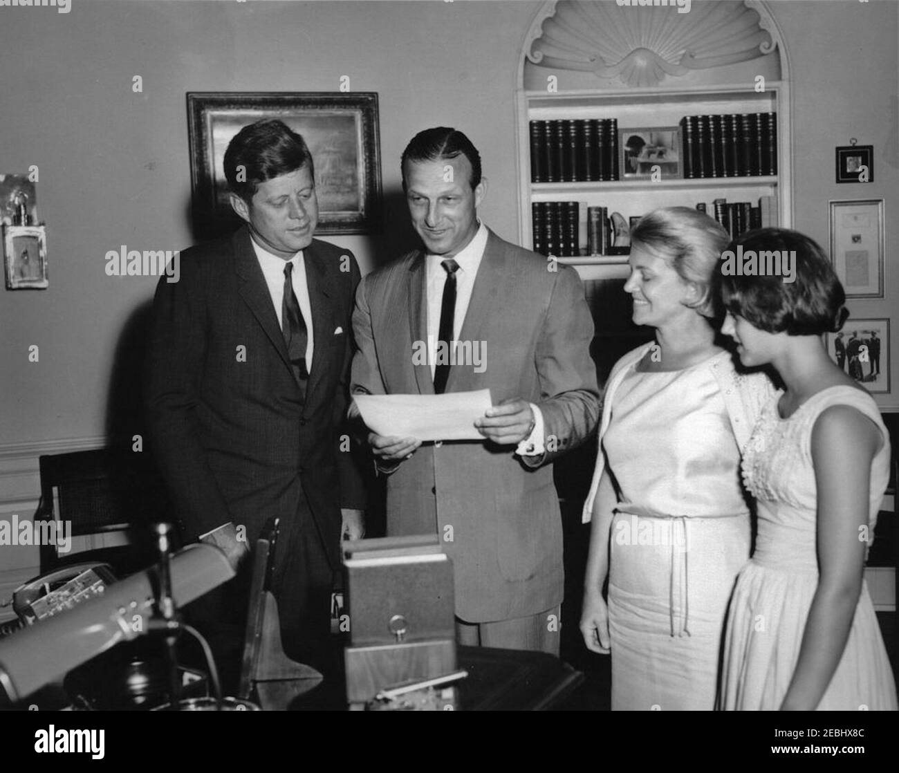 Visite de Stan Musial, joueur de la Ligue majeure de baseball (MLB) pour les Cardinals de Saint-Louis, et de la famille, 4:10. Le président John F. Kennedy et Stan Musial (au centre), joueur de la Ligue majeure de baseball (MLB) pour les Cardinals de St. Louis, regardez une photographie autographiée que le président Kennedy a présentée à M. Musial lors d'une visite dans le Bureau ovale. L'épouse de M. Musialu0027s, Lillian Musial, et sa fille, Janet Musial, regardent de droite. White House, Washington, D.C. Banque D'Images