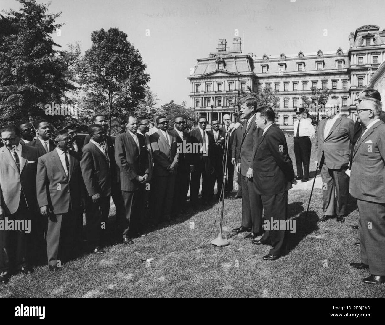 Visite des participants à l'Institut américain pour la gestion libre du travail, 10:05. Le président John F. Kennedy (à micros) fait des remarques aux participants du programme de formation de l'American Institute for Free Labor Development (AIFLD) à l'intention des dirigeants syndicaux d'Amérique latine et des Caraïbes. Le spécialiste de l'Amérique latine du Département du travail des États-Unis, Joaquin A. Bazan, Jr., est à droite du Président Kennedy; le participant Eric Lloyd Harris, de la Jamaïque (à l'arrière, partiellement caché), est à gauche du Président. Debout à l'extrême droite (L-R): Président de la Fédération américaine du travail et du Congrès du Banque D'Images