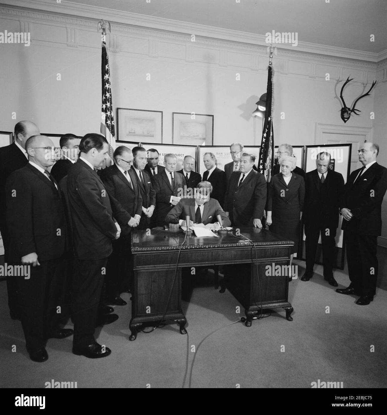 Signature - contrats de remise en état : projet du bassin de Columbia, unité de San Luis, 3:45. Le président John F. Kennedy (assis à son bureau) signe des contrats de remise en état pour deux projets d'irrigation de l'eau, le projet du bassin de Columbia dans l'État de Washington et l'unité de San Luis du projet de la vallée centrale en Californie. Debout (de gauche à droite) : sous-secrétaire de l'intérieur pour le développement de l'eau et de l'énergie, Kenneth Holum (à l'arrière, face cachée); non identifié (à l'avant); secrétaire de l'intérieur, Stewart Udall (à l'arrière); non identifié (à l'avant); représentant Wayne N. Aspinall (Colorado); sénateur Henry M. Banque D'Images