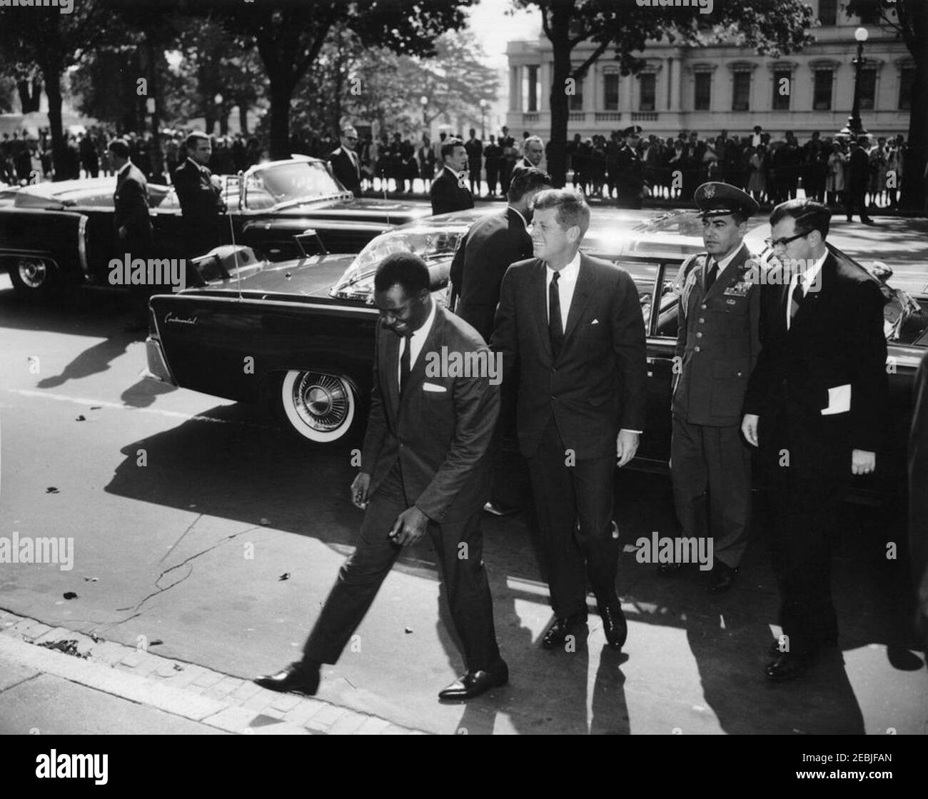 Cérémonie d'arrivée pour Ahmed Su00e9kou Touru00e9, Président de la Guinée, 11 h 00. Le Président John F. Kennedy et le Président de Guinée, Ahmed Su00e9kou Touru00e9 (au centre à gauche), marchent vers Blair House à leur arrivée dans la limousine présidentielle (Lincoln-Mercury Continental convertible avec bulle top), à la suite d'un convoi en l'honneur du Président Touru00e9. L'aide de la Force aérienne au président Kennedy, au brigadier-général Godfrey T. McHugh et à l'interprète du département d'État des États-Unis, Josu00e9 de Seabra, se tiennent à droite. Également en photo : agents du service secret de la Maison Blanche, Ron Pontius, Floyd Boring, John Campi Banque D'Images