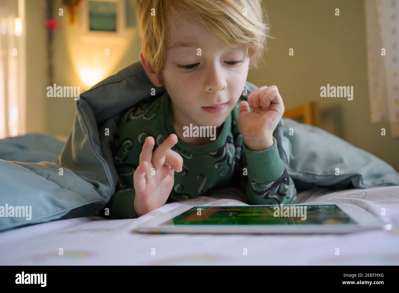 Garçon (6-7) au lit à l'aide d'une tablette numérique Banque D'Images