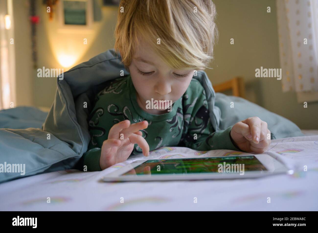 Garçon (6-7) au lit à l'aide d'une tablette numérique Banque D'Images