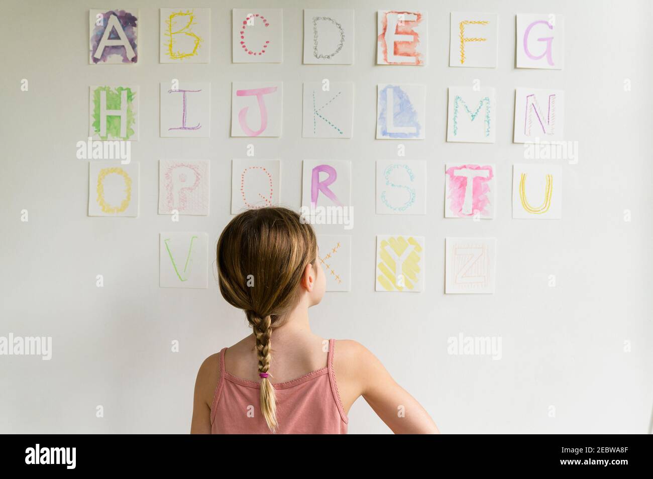 Vue arrière de la fille (8-9) regardant l'alphabet sur le mur Banque D'Images
