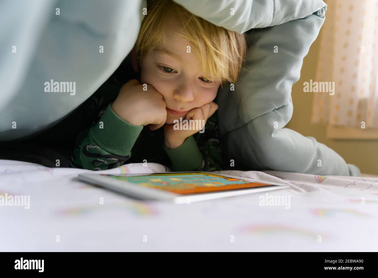 Garçon (6-7) sur le lit regardant la tablette numérique Banque D'Images