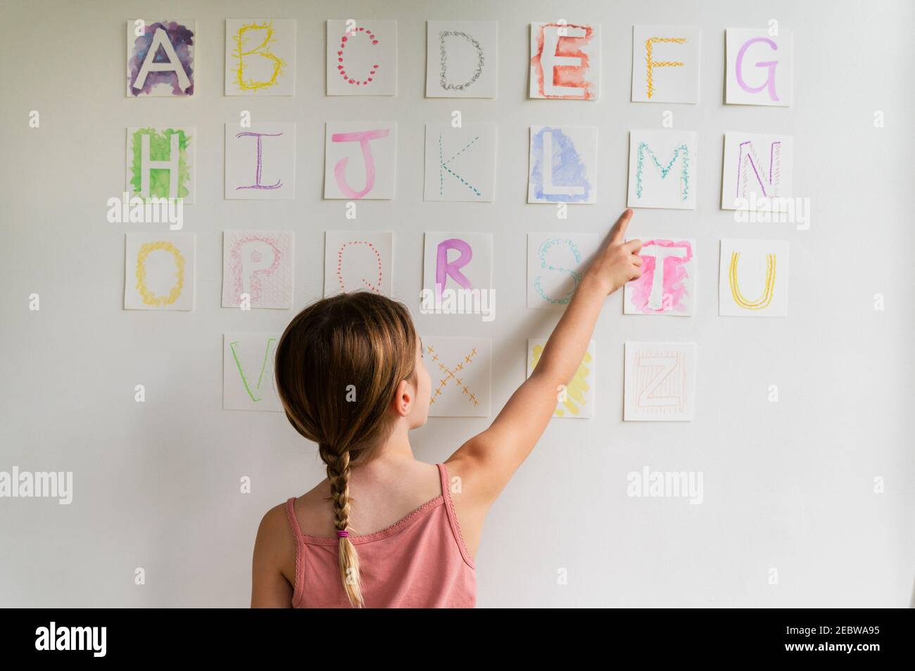 Vue arrière de la fille (8-9) regardant l'alphabet sur le mur Banque D'Images