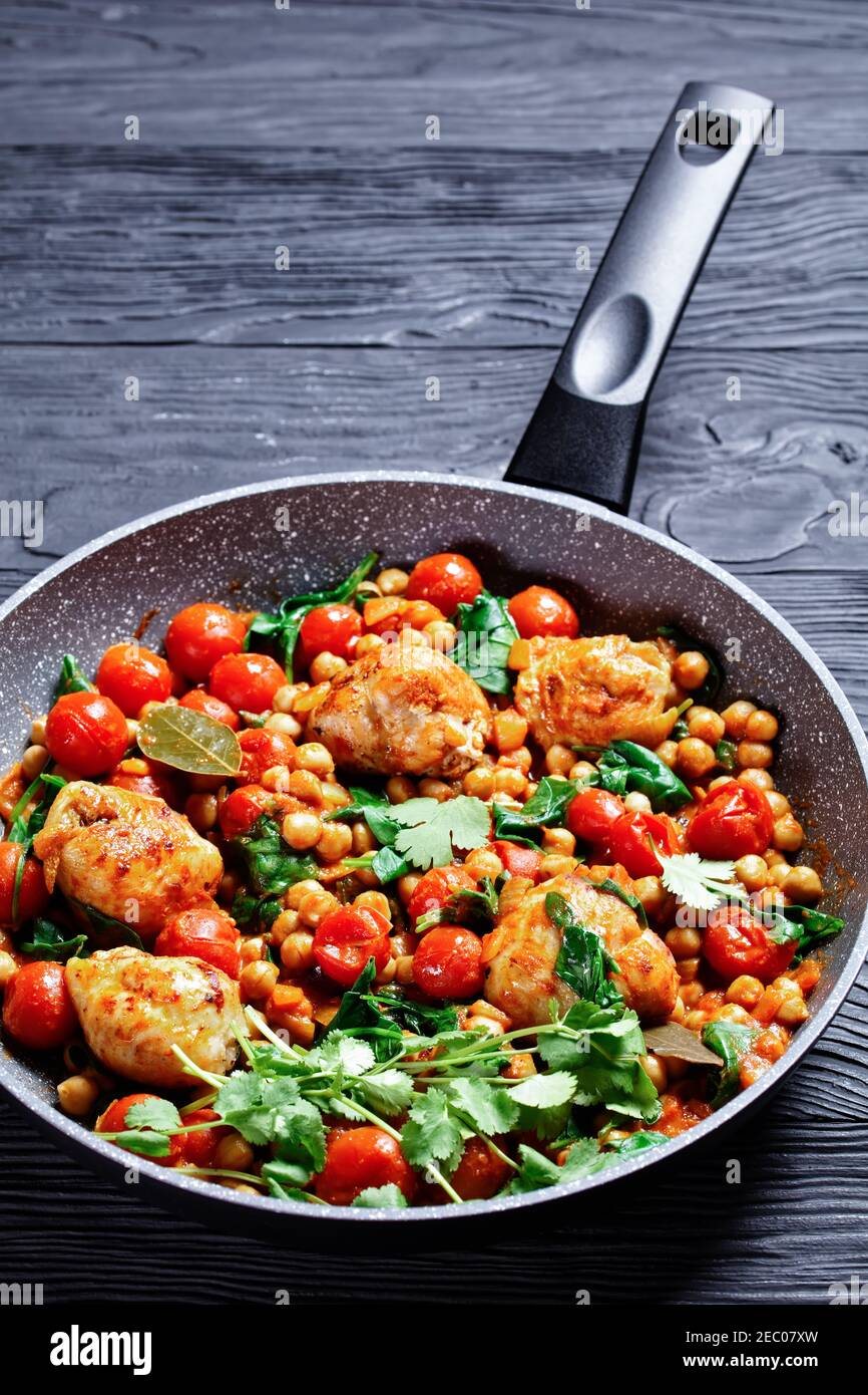 Curry traditionnel de poulet et de pois chiches de cuisses de poulet désossées avec tomates cerises, épinards, gingembre, servi avec de la coriandre fraîche sur une poêle o Banque D'Images