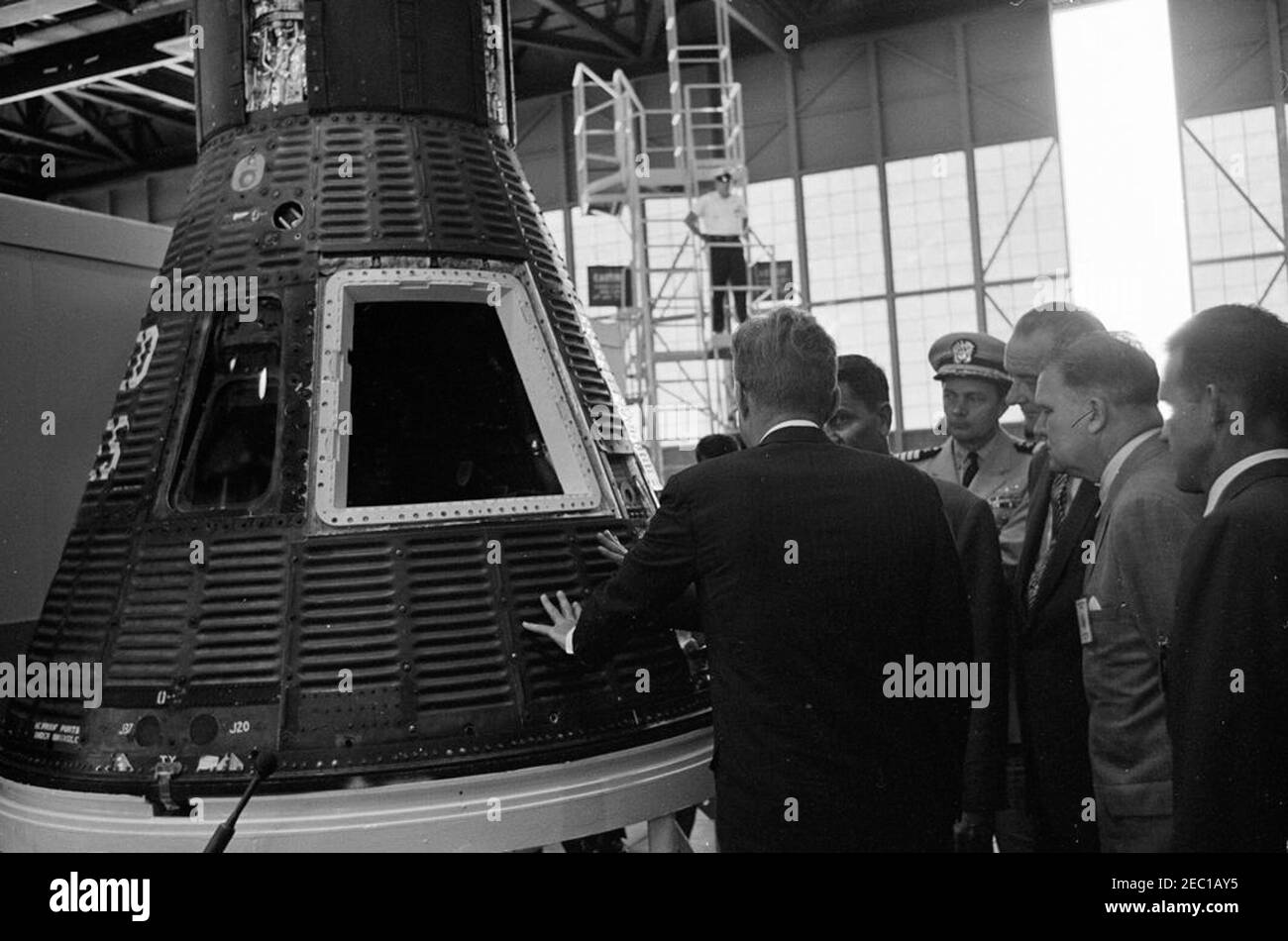 Visite d'inspection des installations de la NASA : Cape Canaveral Florida, 14:31. Le président John F. Kennedy (retour à la caméra) voit la capsule #19 de l'engin spatial Mercury, lors d'une visite des systèmes et de l'équipement Mercury à l'intérieur de Hangar S à la station aérienne de Cape Canaveral, à Cape Canaveral, en Floride; le directeur des opérations de la Floride pour le centre spatial habité, G. Merritt Preston (partiellement caché), en informe le président Kennedy. À l'étude (G-D) : aide navale au président, capitaine Tazewell T. Shepard, Jr.; vice-président Lyndon B. Johnson; administrateur de l'Administration nationale de l'aéronautique et de l'espace (NASA), Dr Banque D'Images