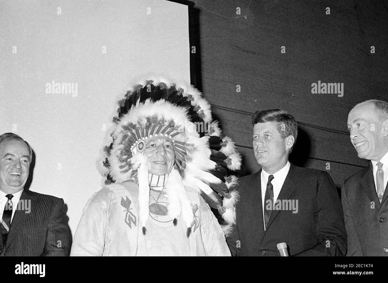Voyage de campagne du Congrès : St. Paul, Minnesota, adresse à The Bean Feed. Le président John F. Kennedy est aux côtés d'un chef de la nation Red Lake à Red Lake, Minnesota, lors d'une apparition à a Bean Feed dans le cadre d'un voyage de campagne du Congrès au Minnesota. Le sénateur Hubert H. Humphrey (Minnesota) est à l'extrême gauche; le lieutenant-gouverneur du Minnesota, Karl Rolvaag, est à l'extrême droite. Pavillon du bétail, champ de foire de l'État du Minnesota, St. Paul, Minnesota. Banque D'Images
