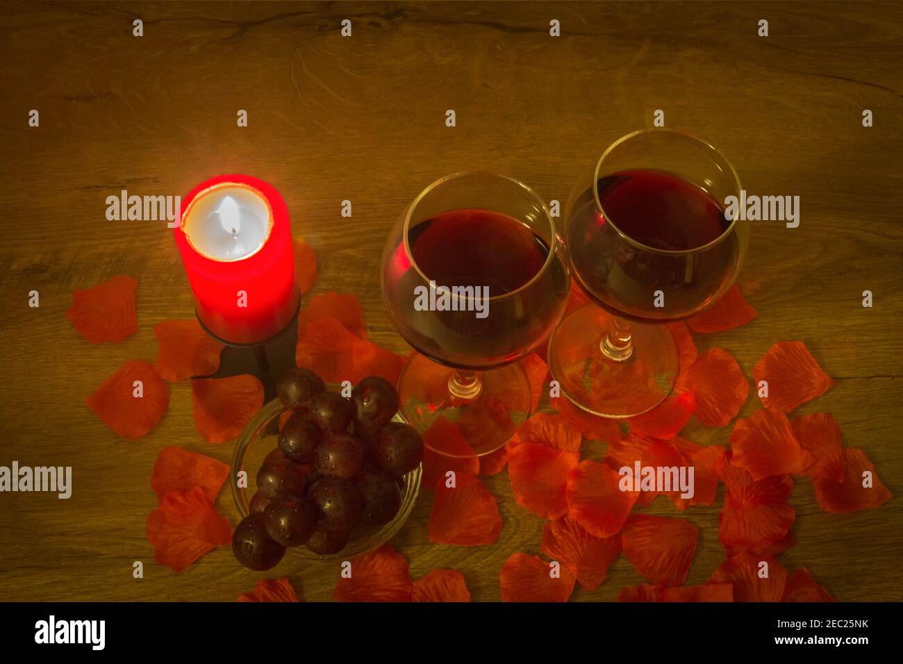Deux verres à vin rouge, du raisin, une bougie en feu et des feuilles de rose sur la table. Concept de la Saint-Valentin. Banque D'Images