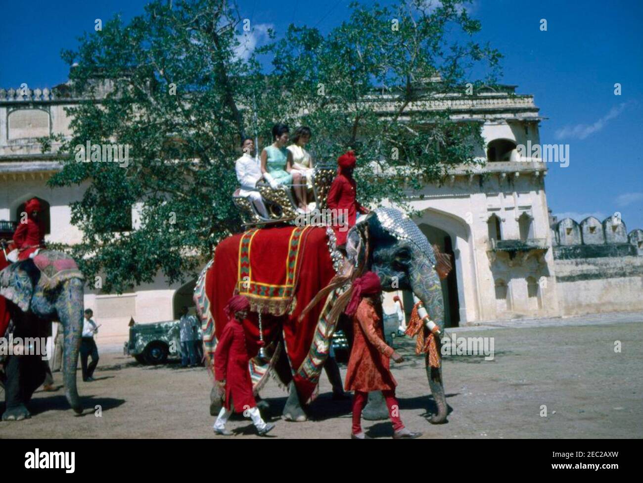 Première Dame Jacqueline Kennedyu2019s (JBK) voyage en Inde et au Pakistan: Jaipur, Rajasthan, Inde, promenade à dos d'éléphant au Palais Amber. La première dame Jacqueline Kennedy (portant une robe jaune) et sa sœur la princesse Lee Radziwill de Pologne, montez à bord d'un éléphant, Bibia, dans la cour du Palais Amber, Jaipur, Rajasthan, Inde. Le ministre de l'intérieur du Rajasthan, Mathura Das Mathur, est assis derrière la princesse Radziwill. Banque D'Images
