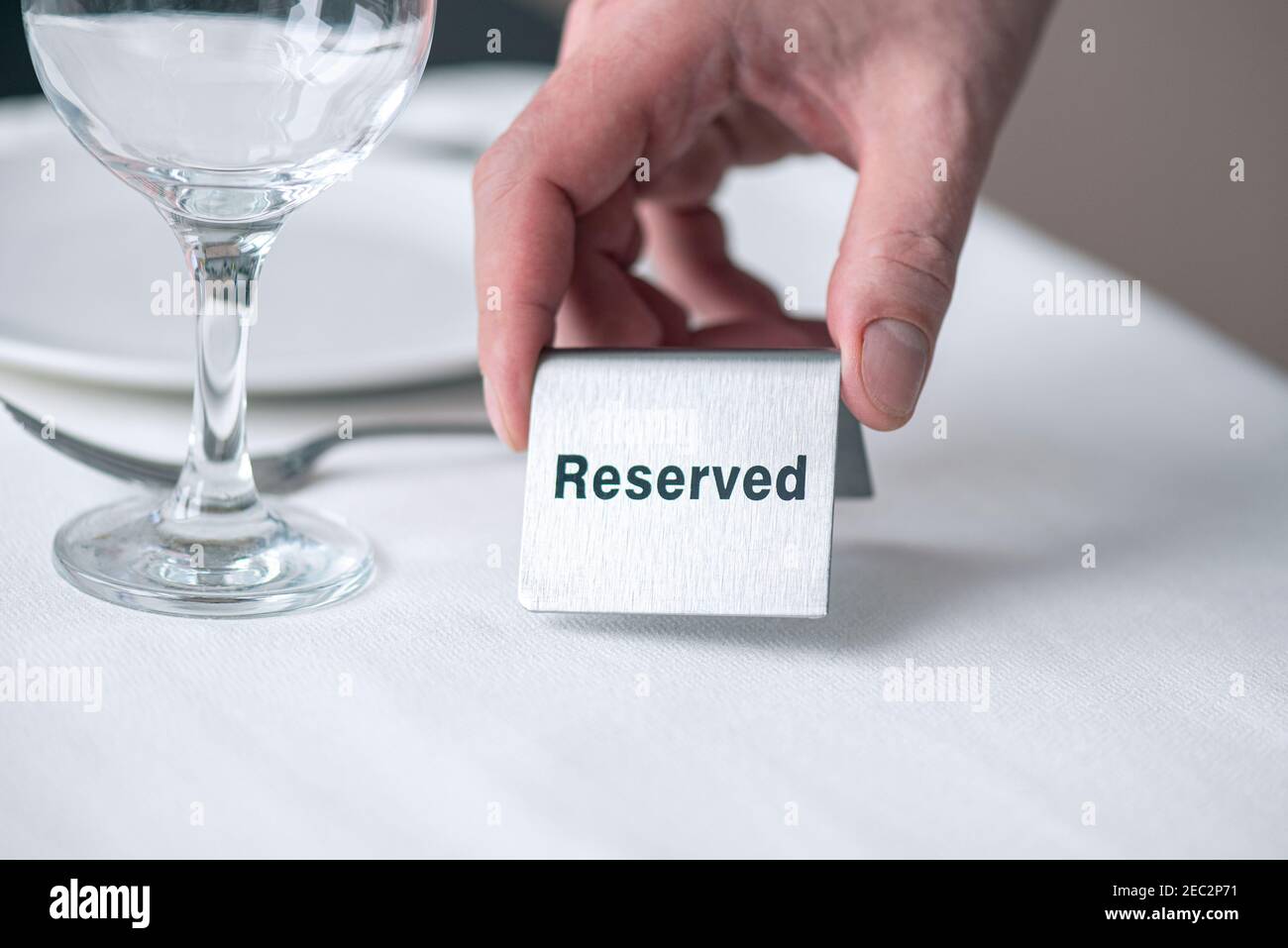 Un serveur tenant une enseigne en fer avec du texte réservé sur la table avec nappe blanche au restaurant Banque D'Images Un serveur tenant une enseigne en fer avec du texte réservé sur la table avec nappe blanche au restaurant Banque D'Images