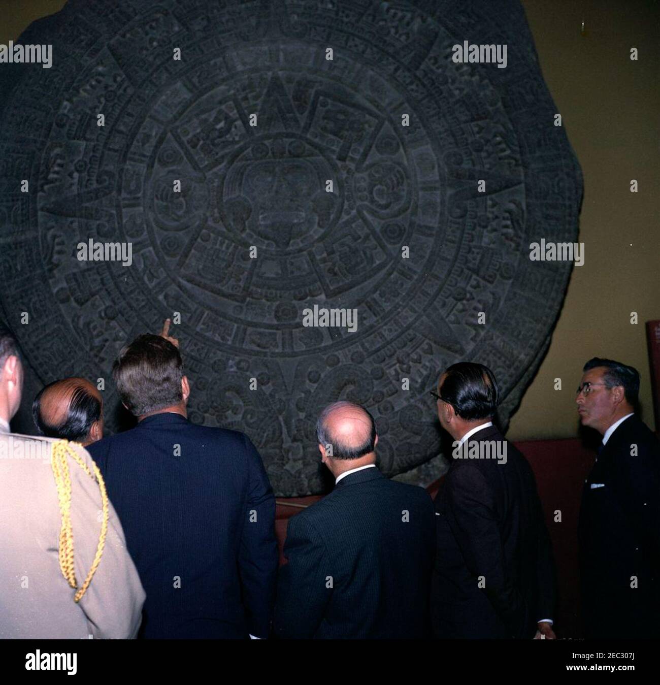 Voyage au Mexique : visite de l'Institut national d'anthropologie et d'histoire, 4:55. Le Président John F. Kennedy voit la Piedra del sol (calendrier aztèque, pierre du Soleil) lors d'une visite du Museo Nacional de Antropologu00eda (Musée national d'anthropologie) de l'Instituto Nacional de Antropologu00eda e Historia (Institut national d'anthropologie et d'histoire) à Mexico, Mexique. De gauche à droite : l'aide militaire au président Kennedy, le général Chester V. Clifton; le chef du département culturel de l'Instituto Nacional de Antropologu00eda e Historia, Joaquu00edn Cortina Goribar; le président Kenn Banque D'Images