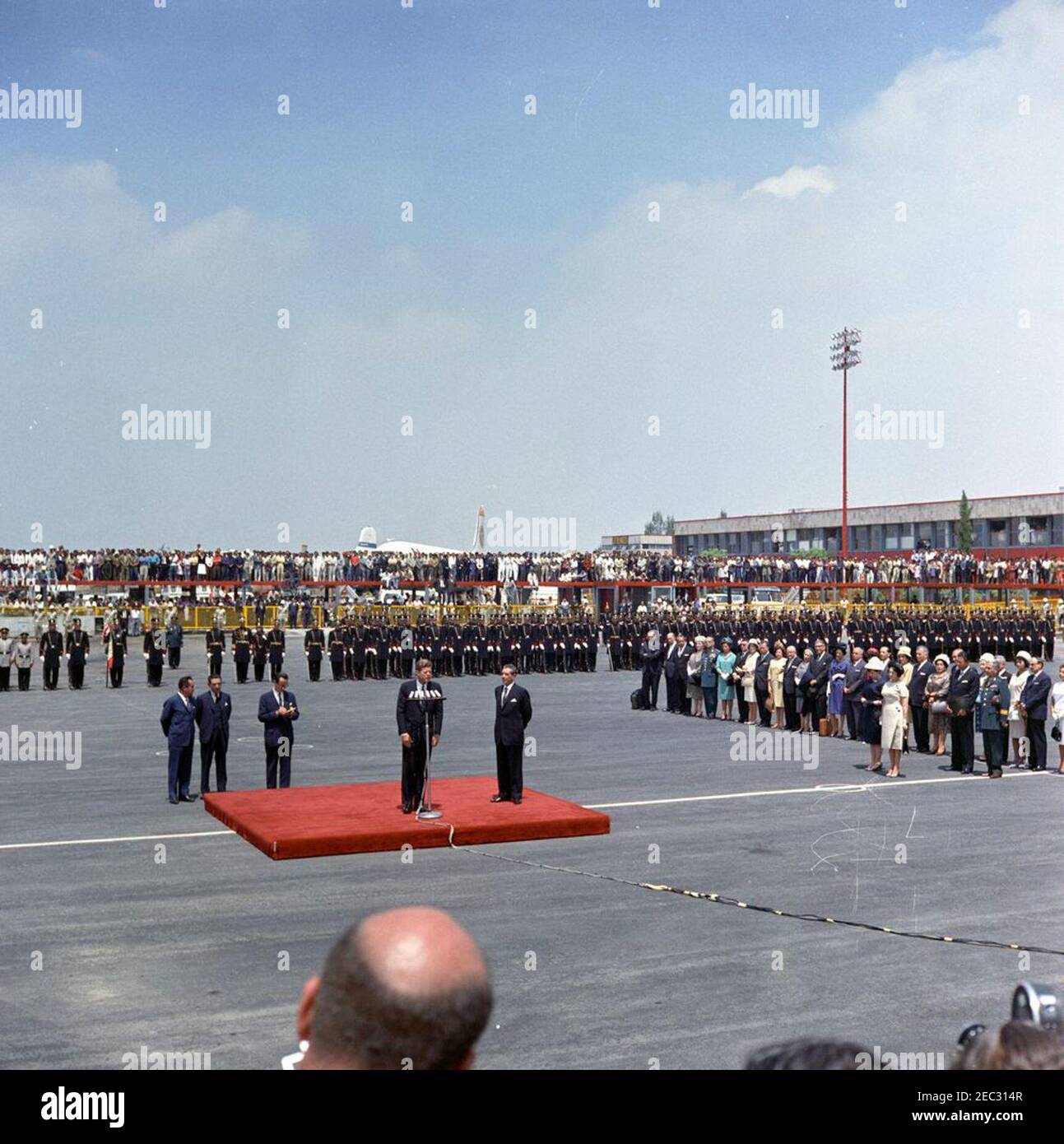 Voyage au Mexique : cérémonies d'arrivée, aéroport international de Mexico, Mexico, Mexique, 11:00. Le président John F. Kennedy (à micros) prononce des remarques à son arrivée à Mexico. Le président du Mexique, Adolfo Lu00f3pez Mateos, est sur la plate-forme à droite. Également photographié : Chef du Protocole du Mexique, Federico A. Mariscal; interprète du Département d'État des États-Unis, Donald Barnes; adjoint spécial du Président du Mexique, Justo Sierra; Directeur général de l'Institut de sécurité sociale du Mexique, Benito Coquet; Fanny Gamboa de Carrillo Flores; Ambassadeur du Mexique aux États-Unis, A Banque D'Images