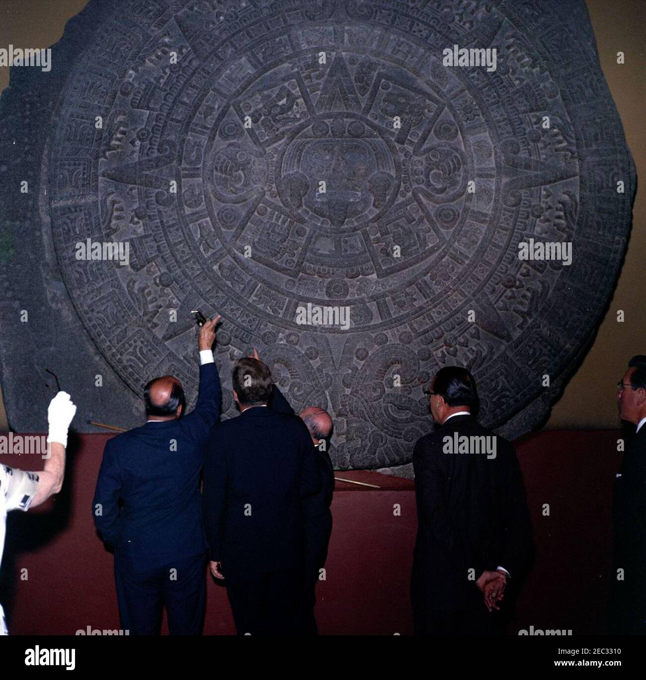 Voyage au Mexique : visite de l'Institut national d'anthropologie et d'histoire, 4:55. Le Président John F. Kennedy voit la Piedra del sol (calendrier aztèque, pierre du Soleil) lors d'une visite du Museo Nacional de Antropologu00eda (Musée national d'anthropologie) de l'Instituto Nacional de Antropologu00eda e Historia (Institut national d'anthropologie et d'histoire) à Mexico, Mexique. De gauche à droite : Chef du Département culturel de l'Instituto Nacional de Antropologu00eda e Historia, Joaquu00edn Cortina Goribar; Président Kennedy; non identifié (pour la plupart caché); Directeur de l'Instituto NAC Banque D'Images