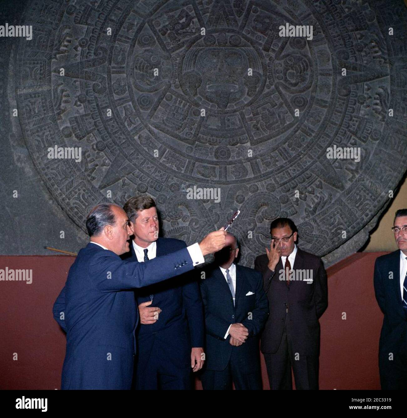 Voyage au Mexique : visite de l'Institut national d'anthropologie et d'histoire, 4:55. Le Président John F. Kennedy se tient devant la Piedra del sol (calendrier aztèque, pierre du Soleil) lors d'une visite au Museo Nacional de Antropologu00eda (Musée national d'anthropologie) de l'Instituto Nacional de Antropologu00eda e Historia (Institut national d'anthropologie et d'histoire) à Mexico, au Mexique. De gauche à droite : Chef du Département culturel de l'Instituto Nacional de Antropologu00eda e Historia, Joaquu00edn Cortina Goribar; Président Kennedy; non identifié; Directeur de l'Instituto Nacio Banque D'Images