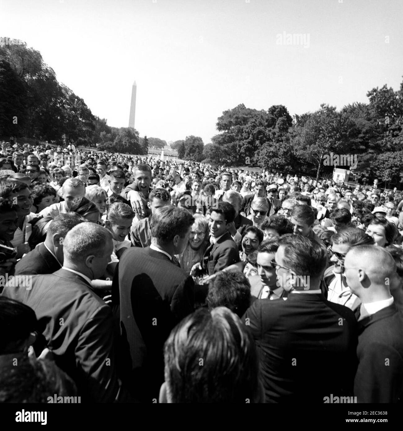 Visite des étudiants du service après-vente américain, 9:50. Le président John F. Kennedy (au centre à gauche, en premier plan) visite des étudiants de l'American Field Service (AFS) sur la pelouse sud de la Maison Blanche, Washington, D.C. l'agent du service secret de la Maison Blanche, Ernest u201cErnieu201d Olsson, se trouve à droite. Le Washington Monument et le Jefferson Memorial sont visibles au loin. Banque D'Images