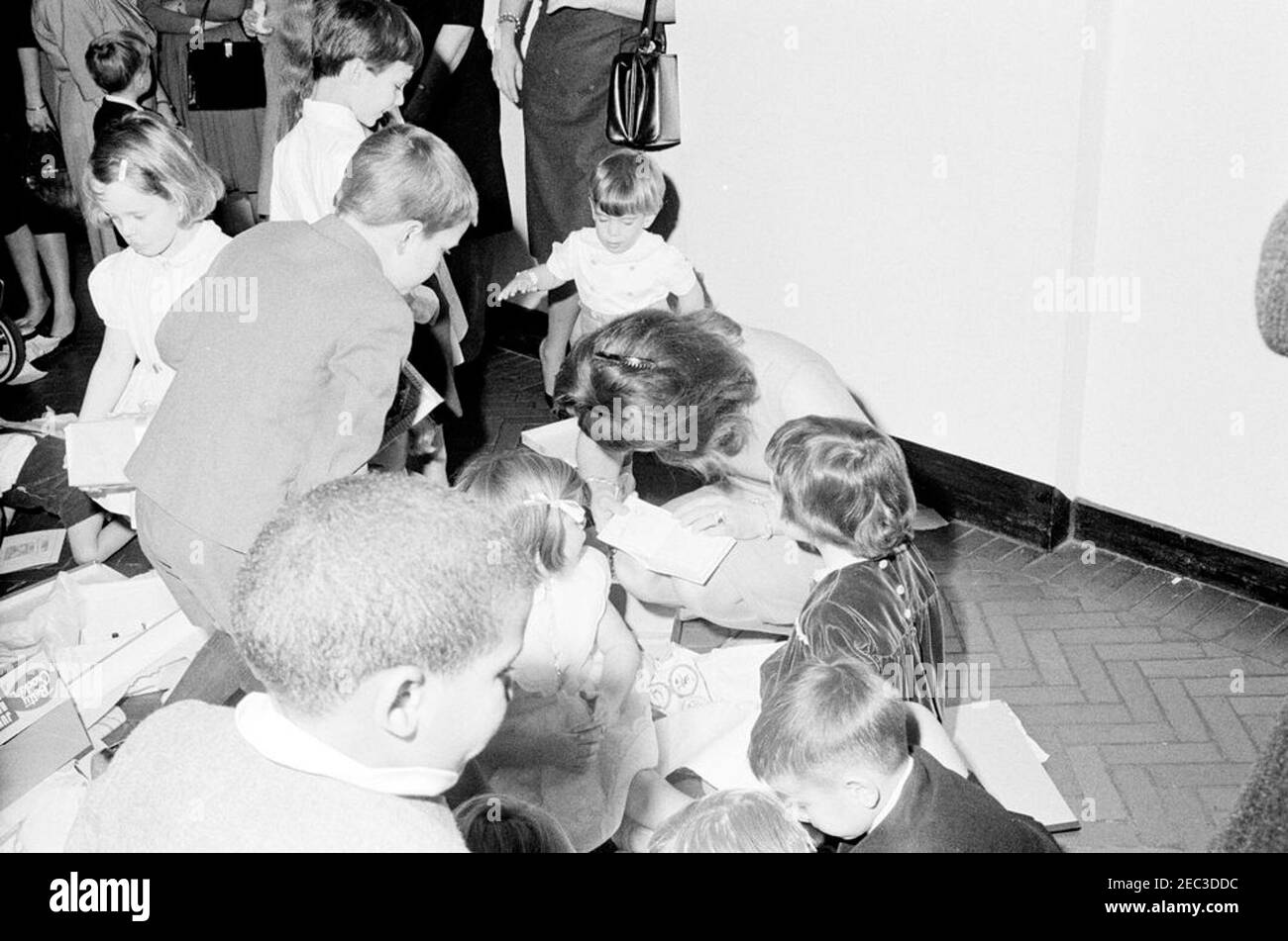 Fête d'anniversaire pour Caroline Kennedy et John F. Kennedy, Jr. La première dame Jacqueline Kennedy (tête badiquée, en lisant un livre) est assise avec ses enfants, Caroline Kennedy (au centre à gauche, face à face) et John F. Kennedy, Jr. (Debout derrière sa mère), lors d'une fête d'anniversaire conjointe pour les enfants; Avery Hatcher, fils du secrétaire de presse associé Andrew T. Hatcher, se trouve à gauche en premier plan. Couloir de l'aile est, Maison Blanche, Washington, D.C. Banque D'Images