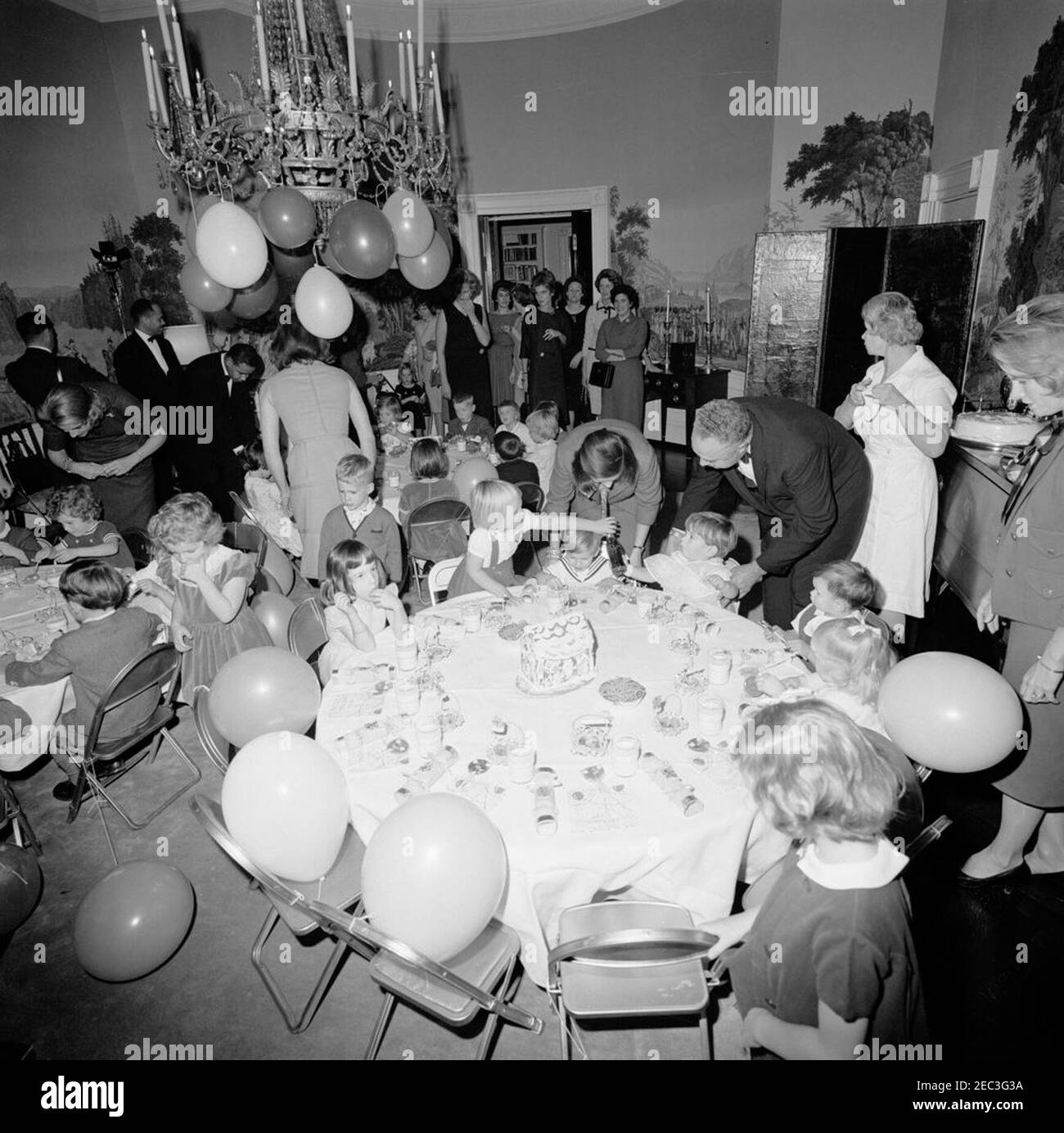 Fête d'anniversaire pour Caroline Kennedy et John F. Kennedy, Jr. De jeunes enfants s'assoient aux tables de la Presidentu2019s Dining Room (Résidence) de la Maison Blanche, Washington, D.C., lors d'une fête d'anniversaire conjointe pour Caroline Kennedy et John F. Kennedy, Jr.; la première dame Jacqueline Kennedy (dos à la caméra) est à gauche. Caroline (au centre à gauche) est assise à la table en arrière-plan avec sa cousine, Maria Shriver (assise en face de Caroline, avec dos à la caméra); John, Jr. (À droite, tenant une bouteille de Coca-Cola), est assise à la table en premier plan. Également en photo : première secrétaire sociale de Ladyu0027s, Letitia Baldrige; W Banque D'Images