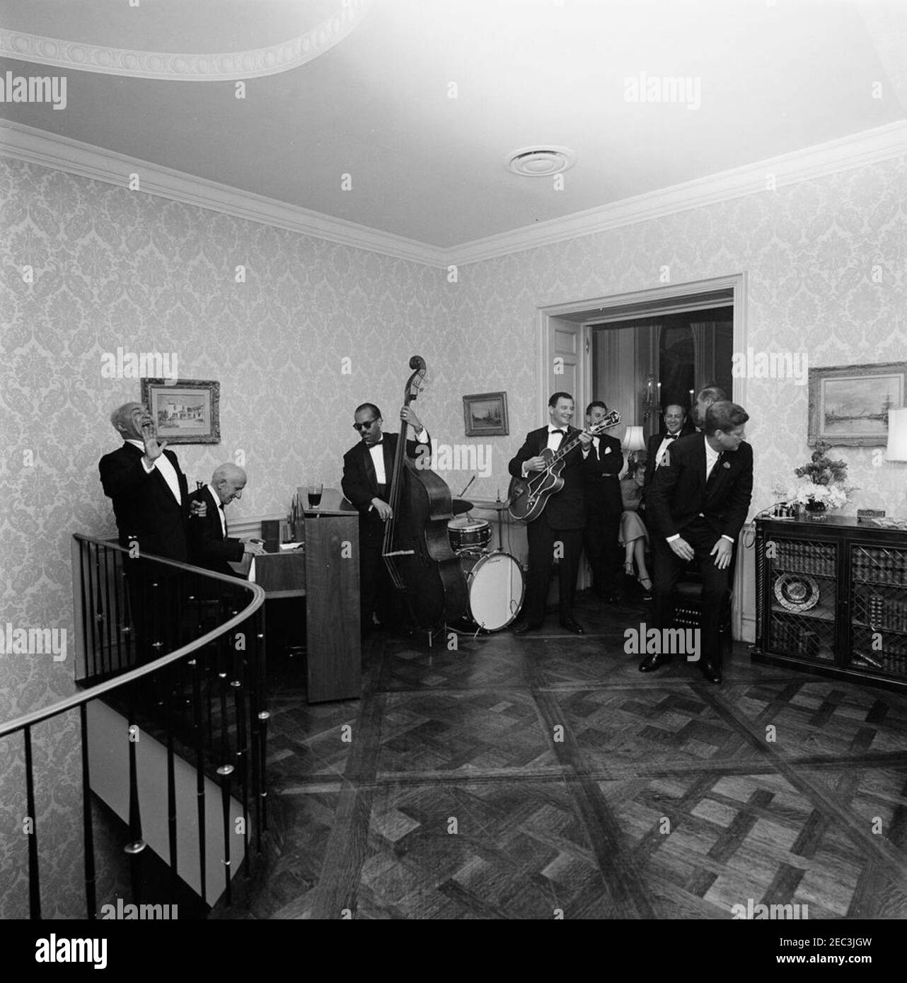 Voyage à New York : réception, résidence Arthur Krim. Le président John F. Kennedy (à l'extrême droite) assiste à une réception en soirée à la résidence d'Arthur B. Krim et du Dr Mathilde Krim, à New York. Des artistes, Jimmy Durante (jouant du piano) et Eddie Jackson (à l'extrême gauche), se produisent avec plusieurs musiciens non identifiés. Banque D'Images Voyage à New York : réception, résidence Arthur Krim. Le président John F. Kennedy (à l'extrême droite) assiste à une réception en soirée à la résidence d'Arthur B. Krim et du Dr Mathilde Krim, à New York. Des artistes, Jimmy Durante (jouant du piano) et Eddie Jackson (à l'extrême gauche), se produisent avec plusieurs musiciens non identifiés. Banque D'Images