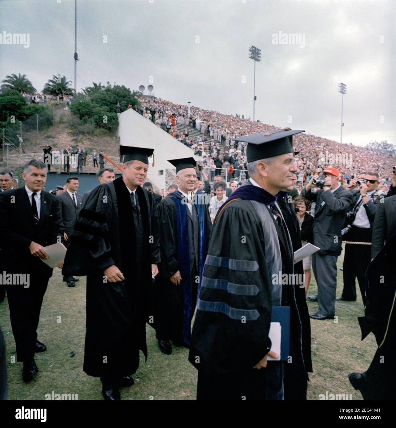 Voyage dans les États de l'Ouest : San Diego, Californie, arrivée à Lindbergh Field, convoi de voitures et adresse de commencement au San Diego State College. Le président John F. Kennedy assiste aux exercices de commencement au San Diego State College. Au premier plan (G-D): Président Kennedy; président du San Diego State College, Dr Malcolm A. Love; chancelier des California State Colleges, Dr Glenn S. Dumke. Debout à gauche (L-R) : les agents du service secret de la Maison Blanche, Roy Kellerman, Gerald A. u201cJerryu201d Behn, Charlie Kunkel et Emory Roberts (au-dessus de l'épaule du président Kennedyu2019s). Aztec Bowl Stadium, San D. Banque D'Images