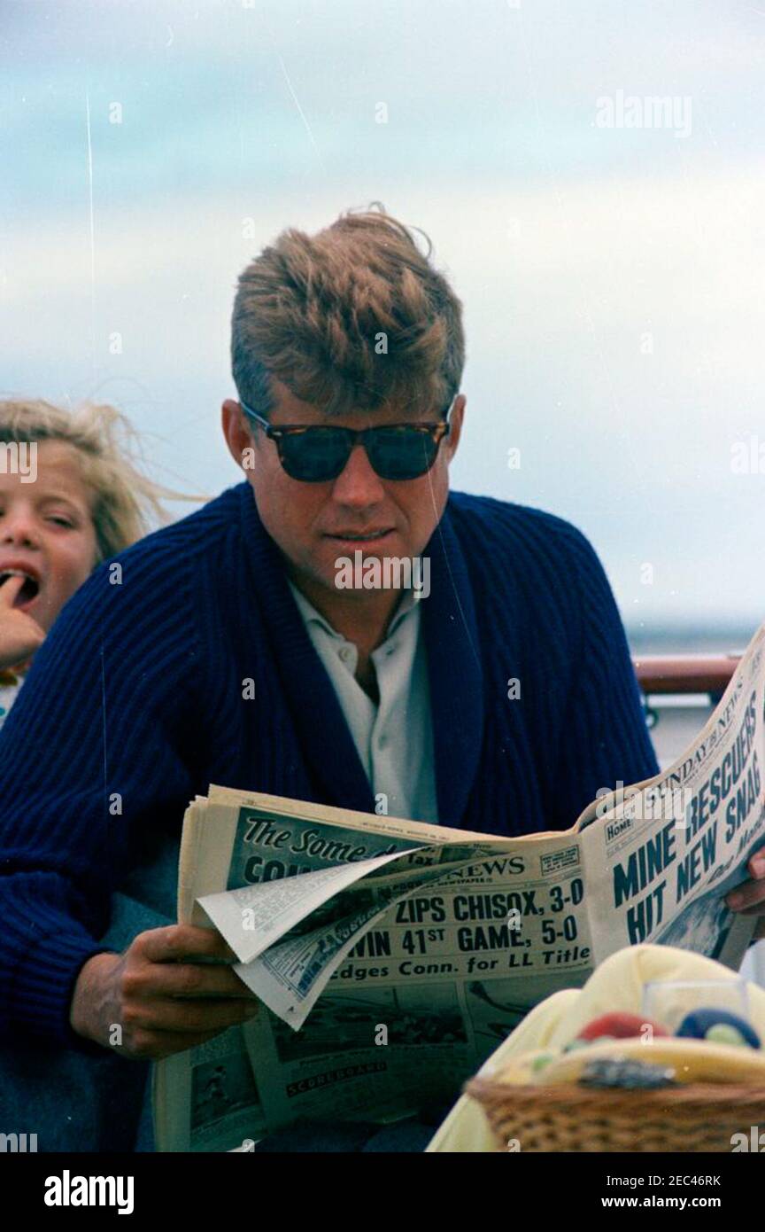 Week-end au port de Hyannis : président Kennedy, Caroline Kennedy (CBK) à  bord d'un yacht. Le président John F. Kennedy (portant des lunettes de  soleil) lit un journal tandis que sa fille,