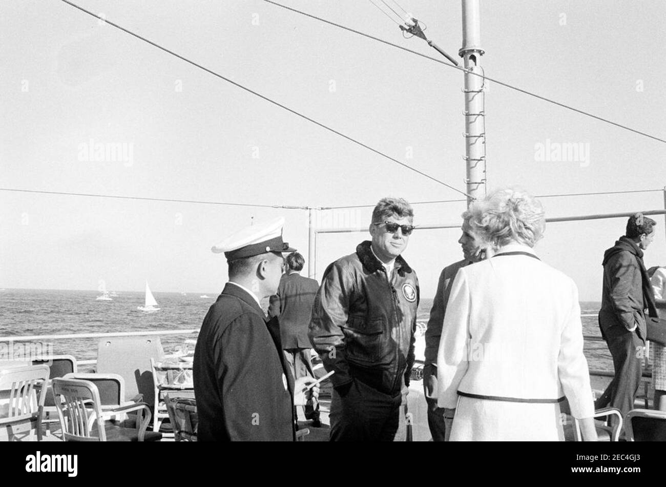 Le Président Kennedy Watches la 1ère course de la coupe Americau0027s. Le président John F. Kennedy (portant des lunettes de soleil) visite le sénateur Benjamin A. Smith II du Massachusetts (pour la plupart caché) et Barbara Mechem Smith (de retour à la caméra) à bord de l'USS Joseph P. Kennedy, Jr., lors de la première course de la coupe Americau0027s de 1962; le sénateur Claiborne Pell (Rhode Island) se trouve tout à droite. Newport, Rhode Island. Banque D'Images