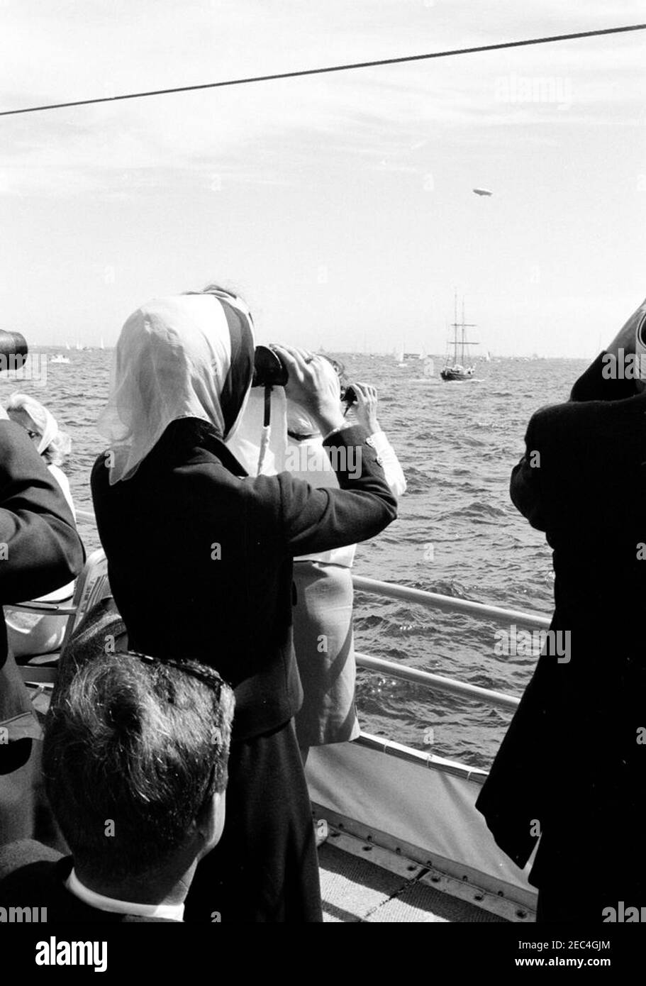 Le Président Kennedy Watches la 1ère course de la coupe Americau0027s. Le président John F. Kennedy (assis en bas à gauche) et la première dame Jacqueline Kennedy (regardant à travers des jumelles) regardent la première course de la coupe Americau0027s 1962 à bord de l'USS Joseph P. Kennedy, Jr., au large de Newport, Rhode Island. Banque D'Images